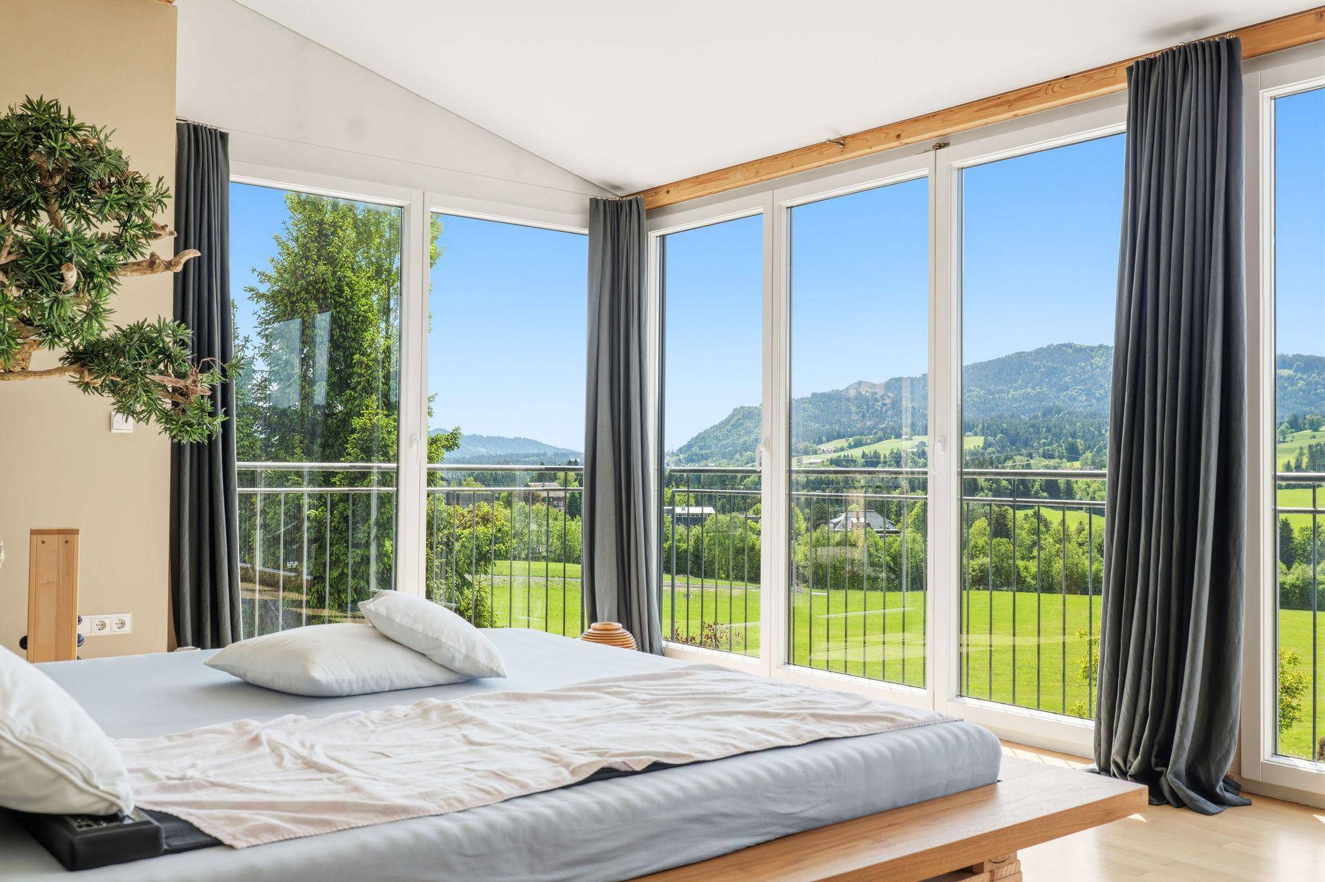 Helles Schlafzimmer mit Holzbett, raumhohen Fenstern und einem atemberaubenden Blick auf die grüne Landschaft.