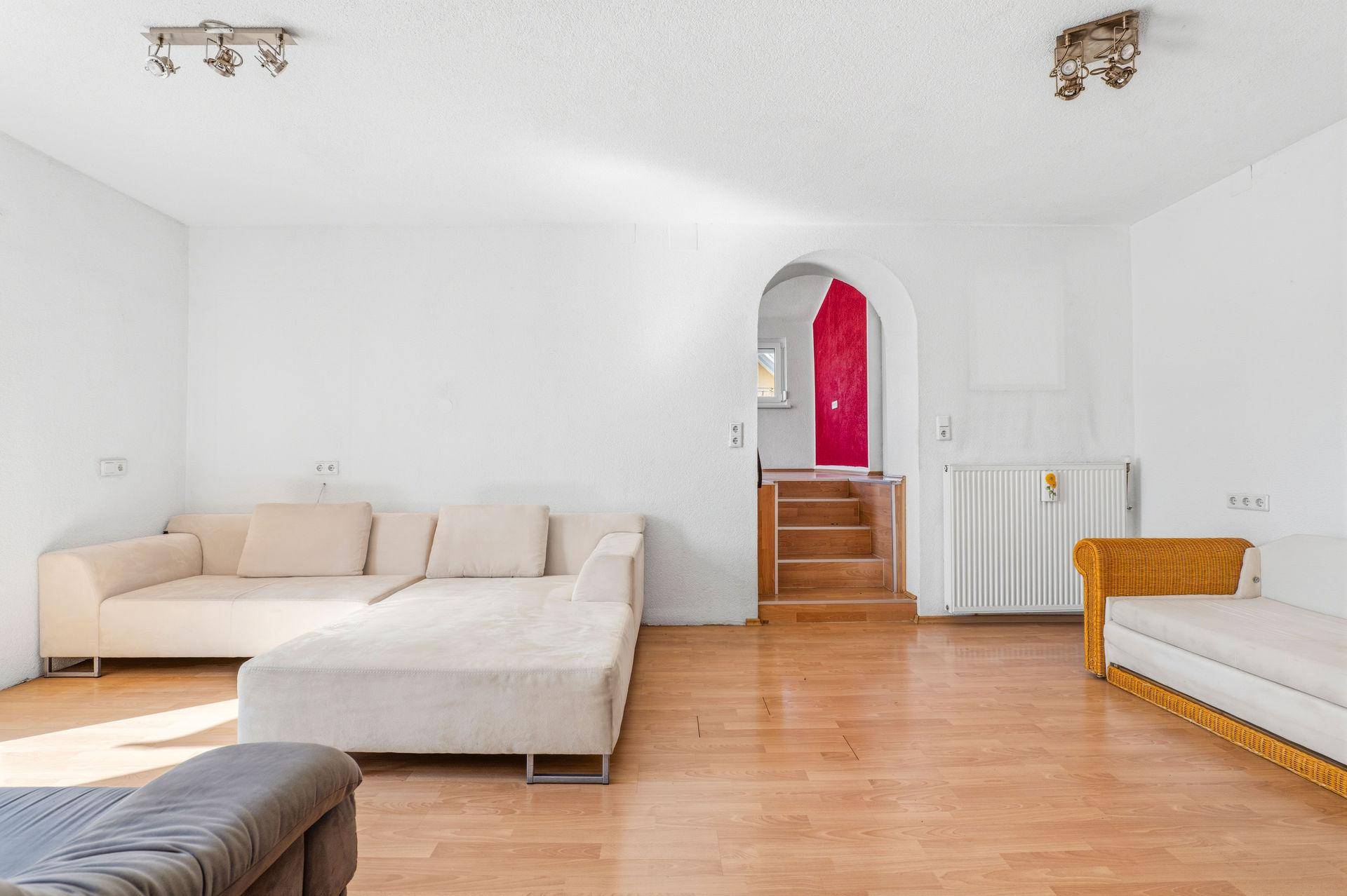 Helles Wohnzimmer mit Parkettboden, beigen Sofas und Zugang zu einer Treppe.