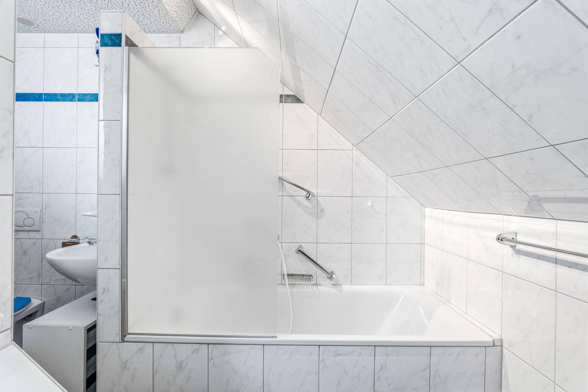 Badezimmer mit Badewanne, Duschabtrennung und schrägen Wänden im Dachgeschoss.