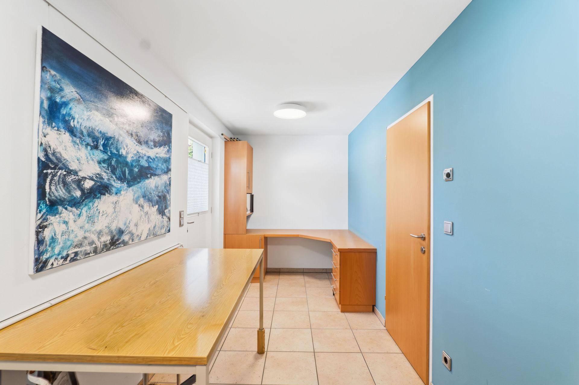 Funktionales Büro mit langem Schreibtisch, blauer Akzentwand und Fliesenboden.
