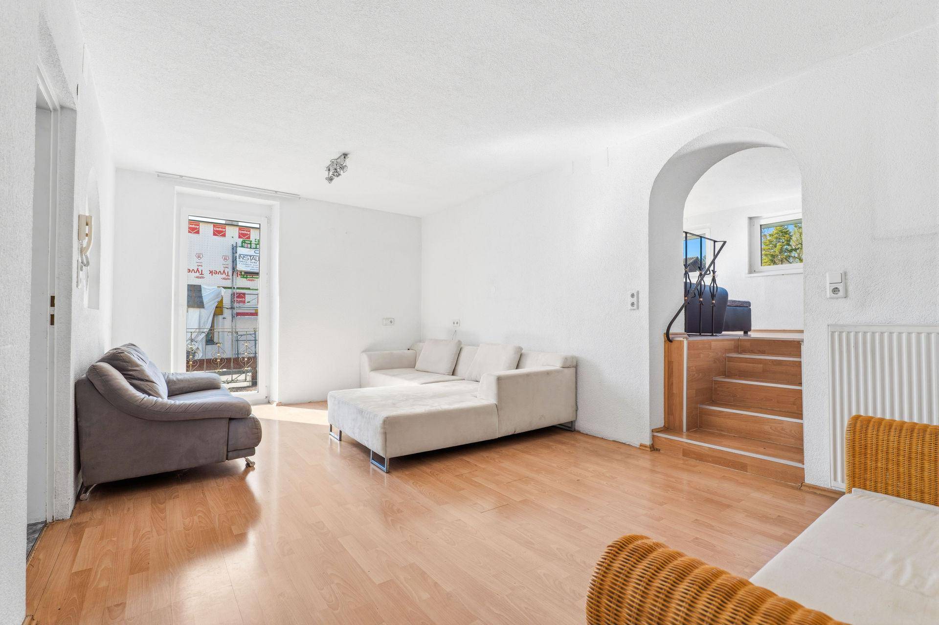 Geräumiges Wohnzimmer mit Parkettboden, beigen Sofas und Blick nach draußen.