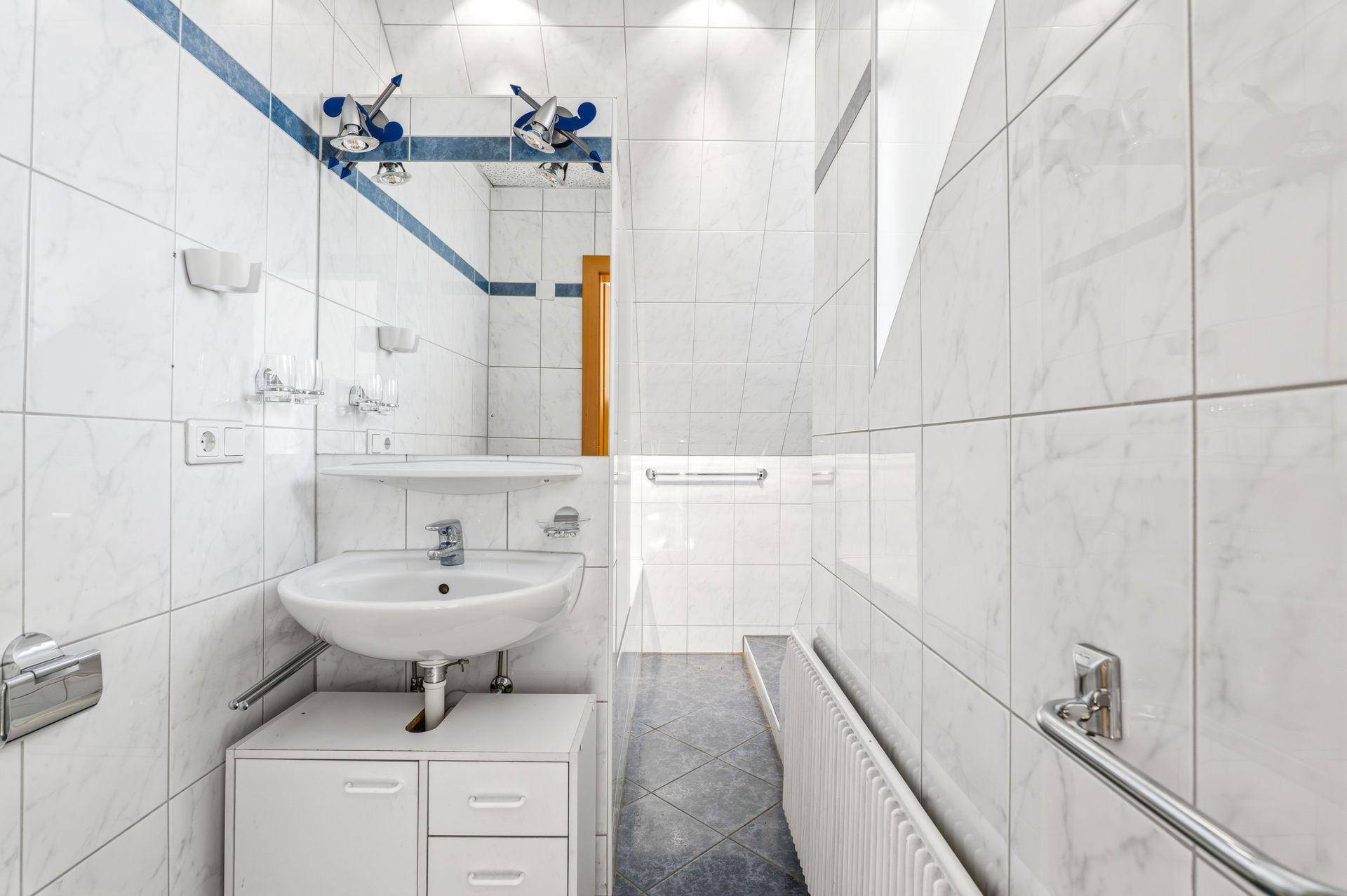 Badezimmer mit blauen und weißen Fliesen, Waschbecken und Heizkörper.
