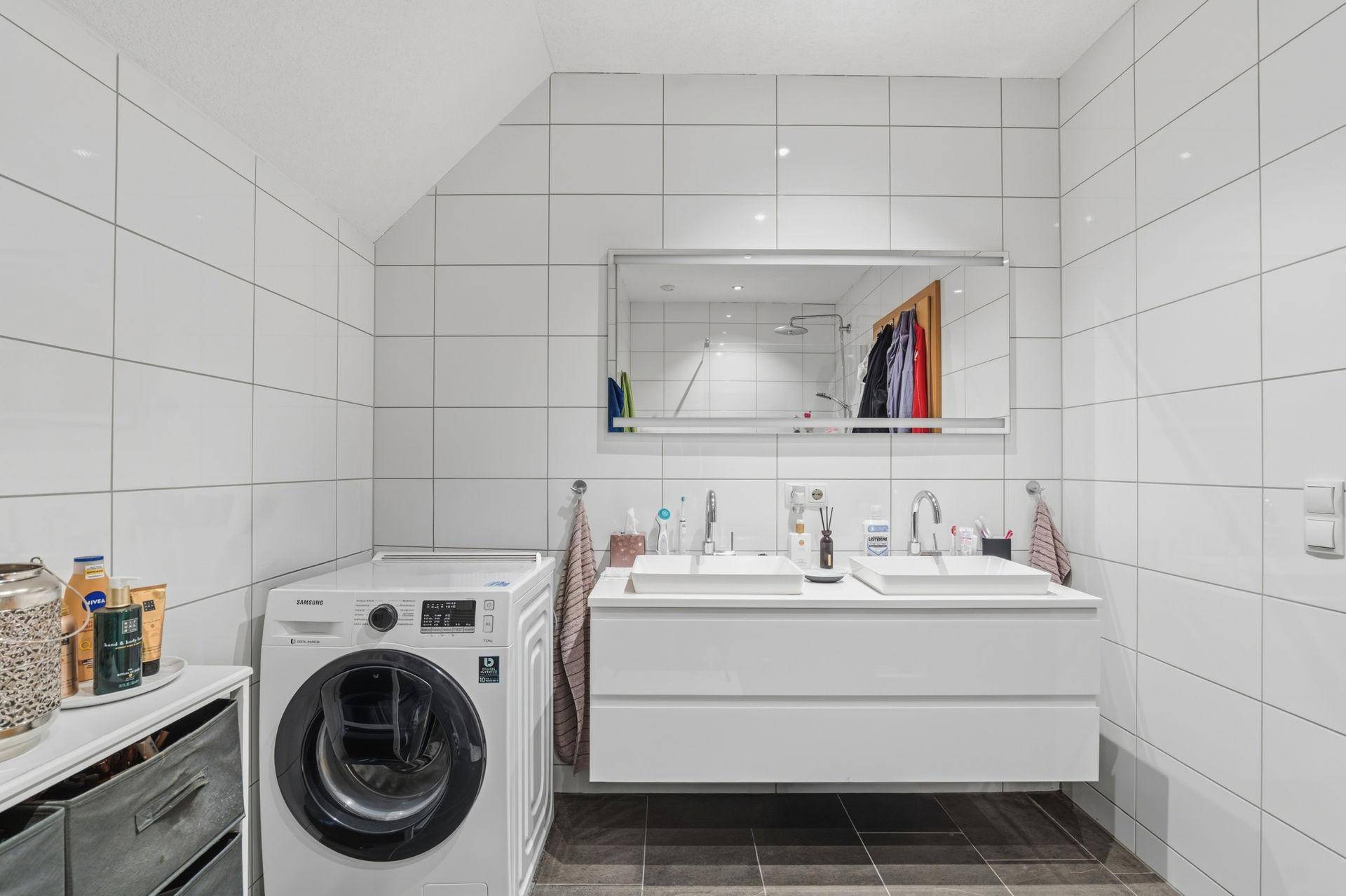 Helles Badezimmer mit Doppelwaschbecken, Waschmaschine und Dachschräge.