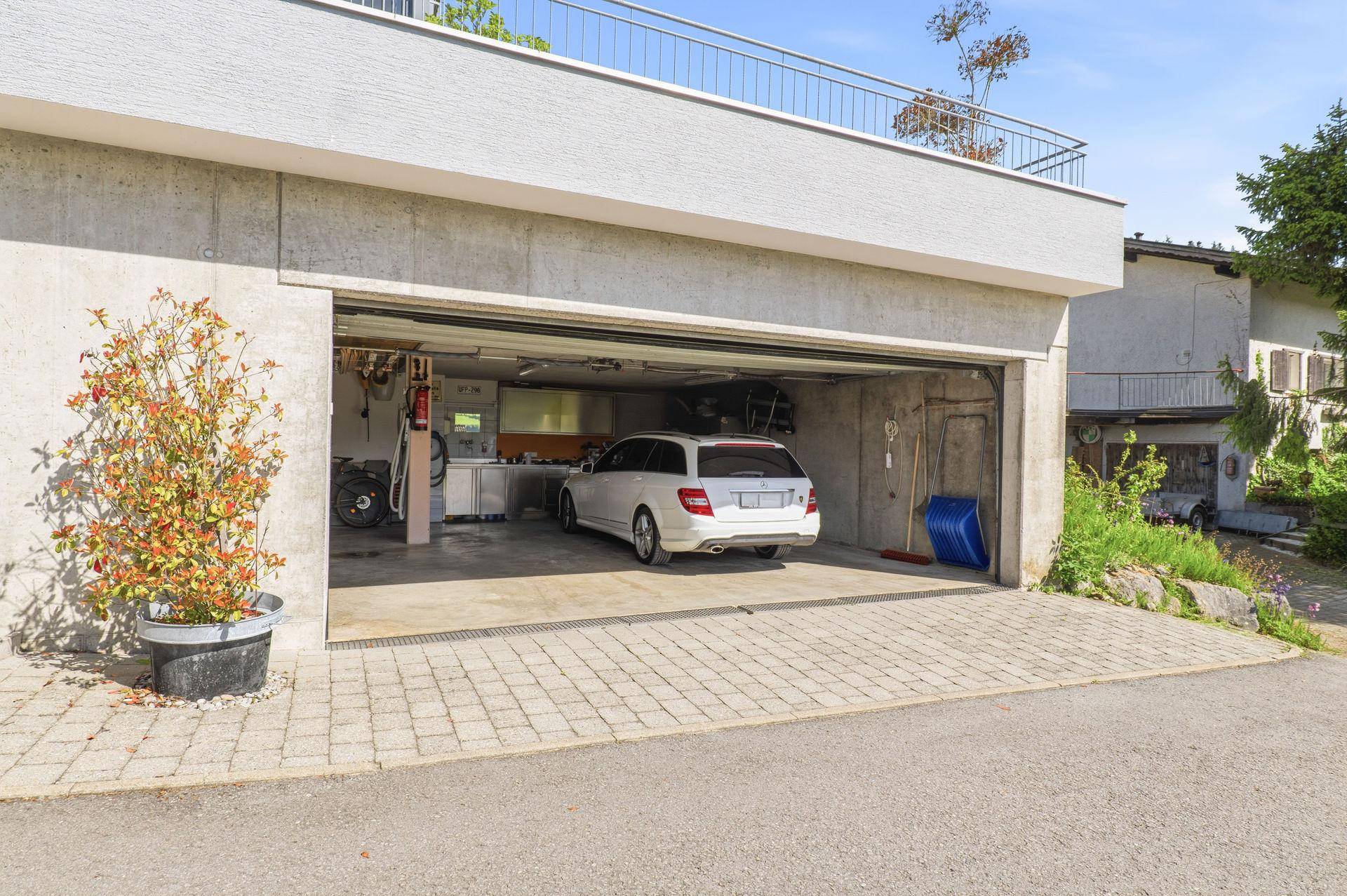 Offene Doppelgarage mit einem geparkten Auto und gepflasterter Zufahrt vor dem Gebäude.