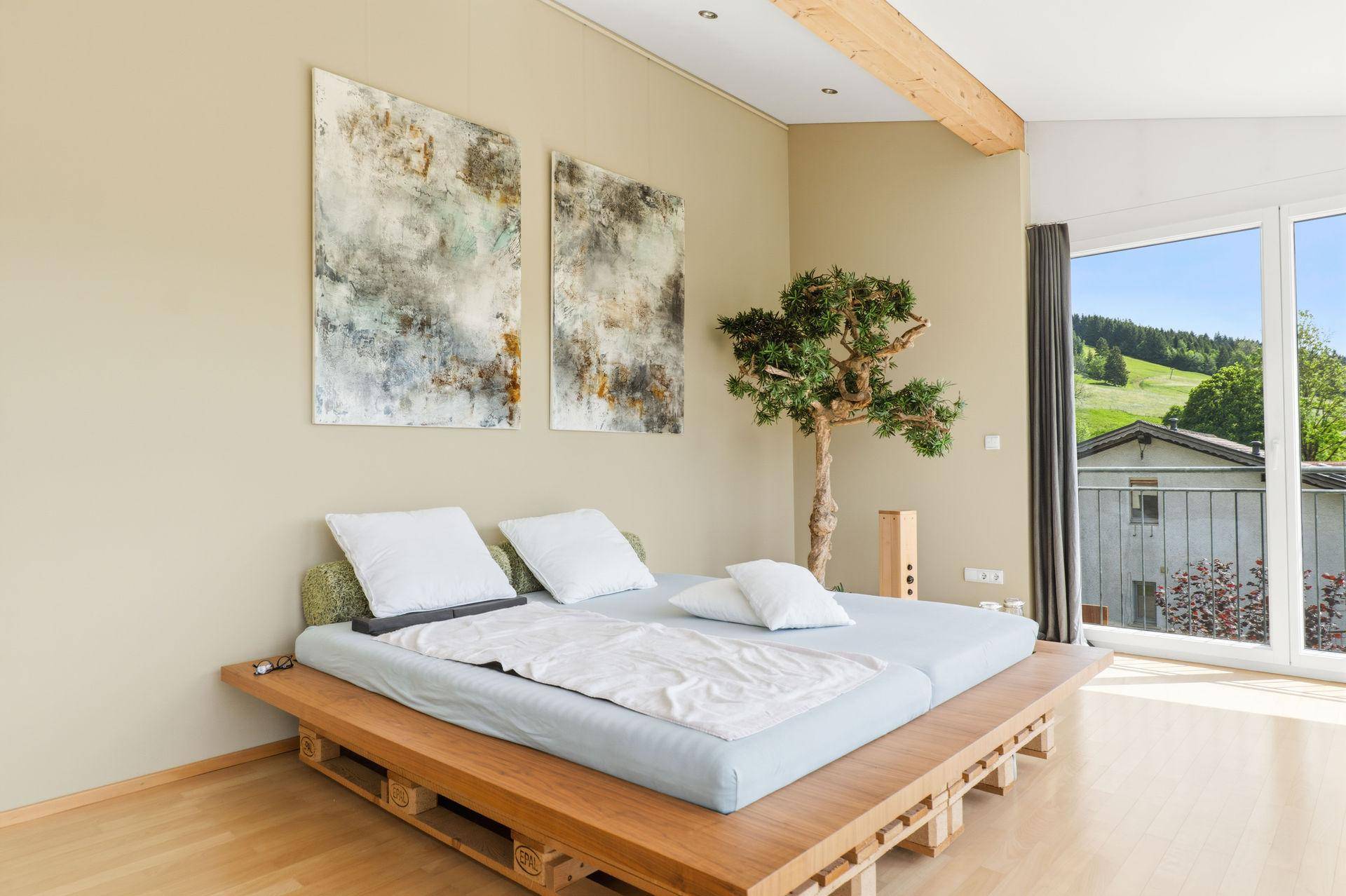 Ruhiges Schlafzimmer mit Holzbett, hellen Wänden und dekorativen Elementen, viel Tageslicht.