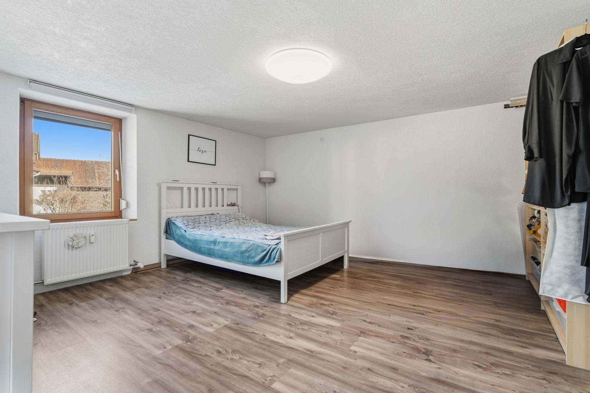 Geräumiges Schlafzimmer mit Holzboden, weißem Bett und offenem Kleiderschrank.