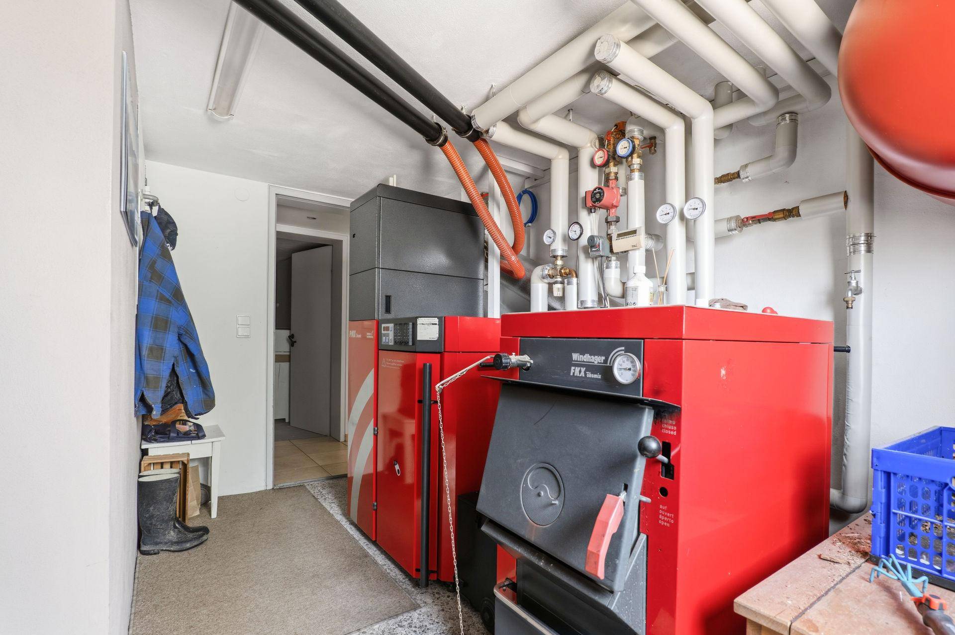 Funktionaler Heizungsraum mit großen roten Heizkesseln, sichtbaren Rohrleitungen und Lagerbereich.
