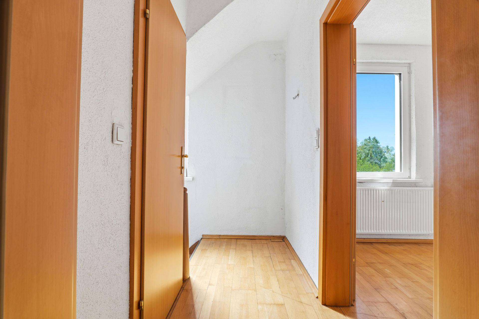 Flur mit Parkettboden, der zu einem hellen Schlafzimmer mit Fenster führt.