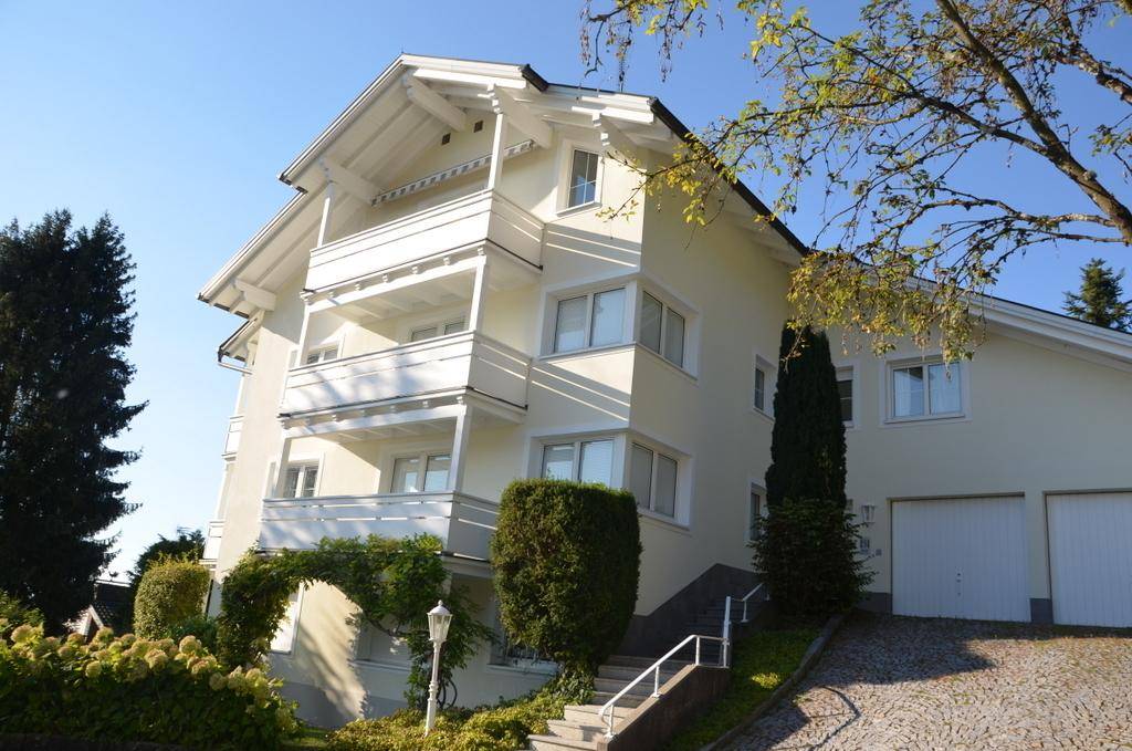 Helles Wohngebäude mit Balkonen, Garage und gepflegtem Vorgarten an einem sonnigen Tag.
