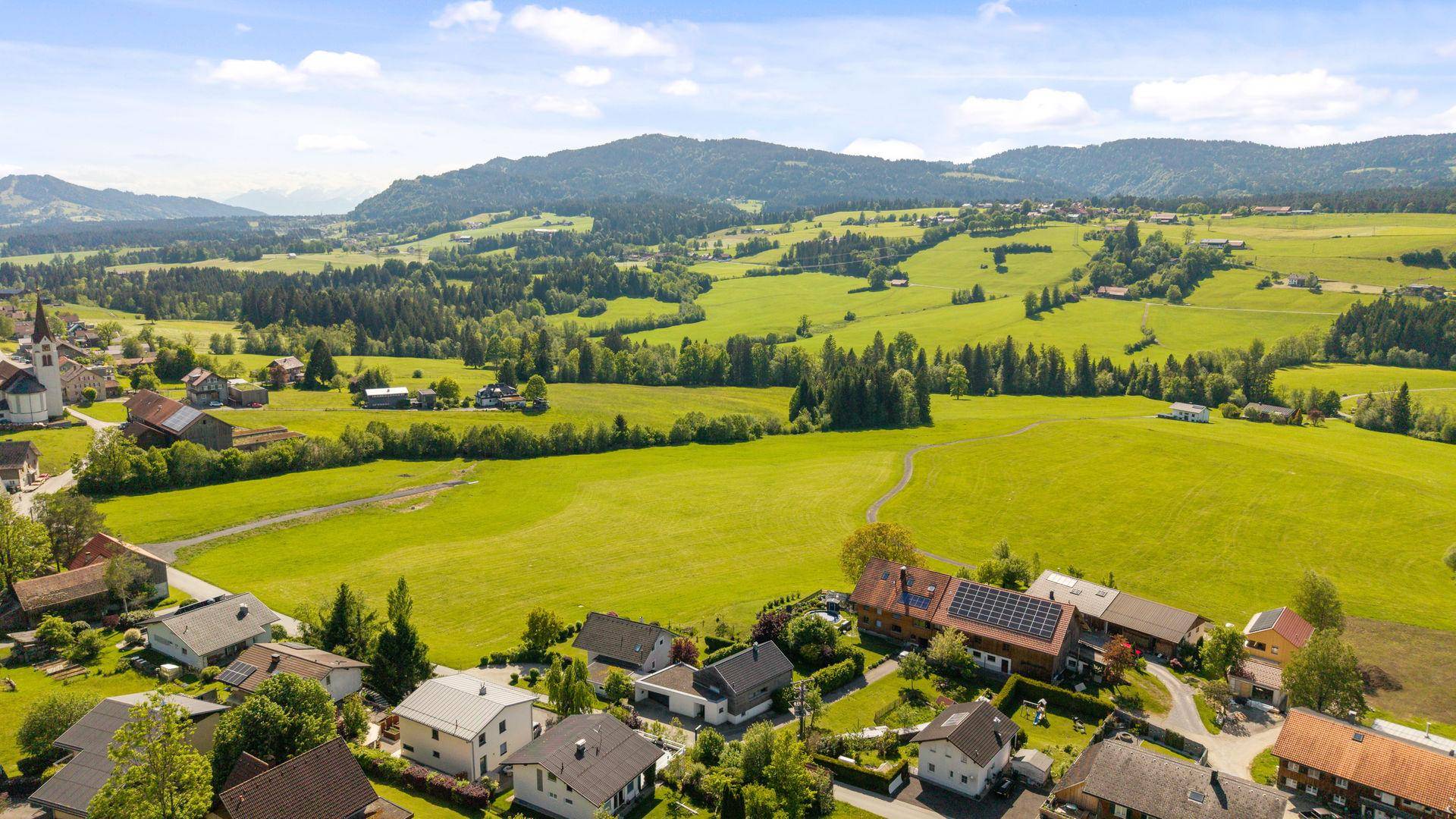Panoramablick aus der Luft auf eine ländliche Gegend mit Häusern, Wiesen und bewaldeten Hügeln.