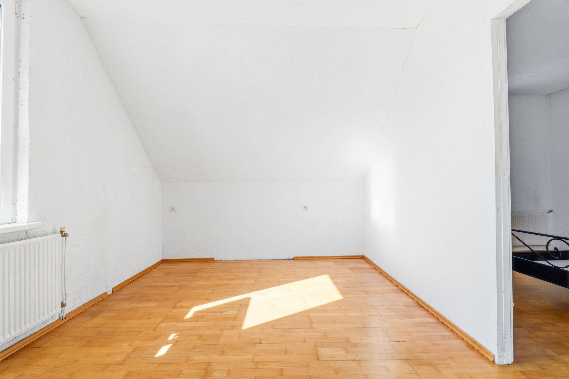 Helles Schlafzimmer im Dachgeschoss mit Holzboden, Dachschräge und viel Tageslicht.