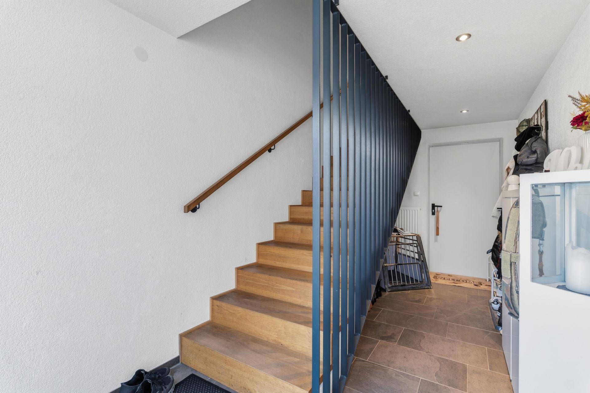 Eingangsbereich mit Holztreppe, modernem Geländer und Fliesenboden.