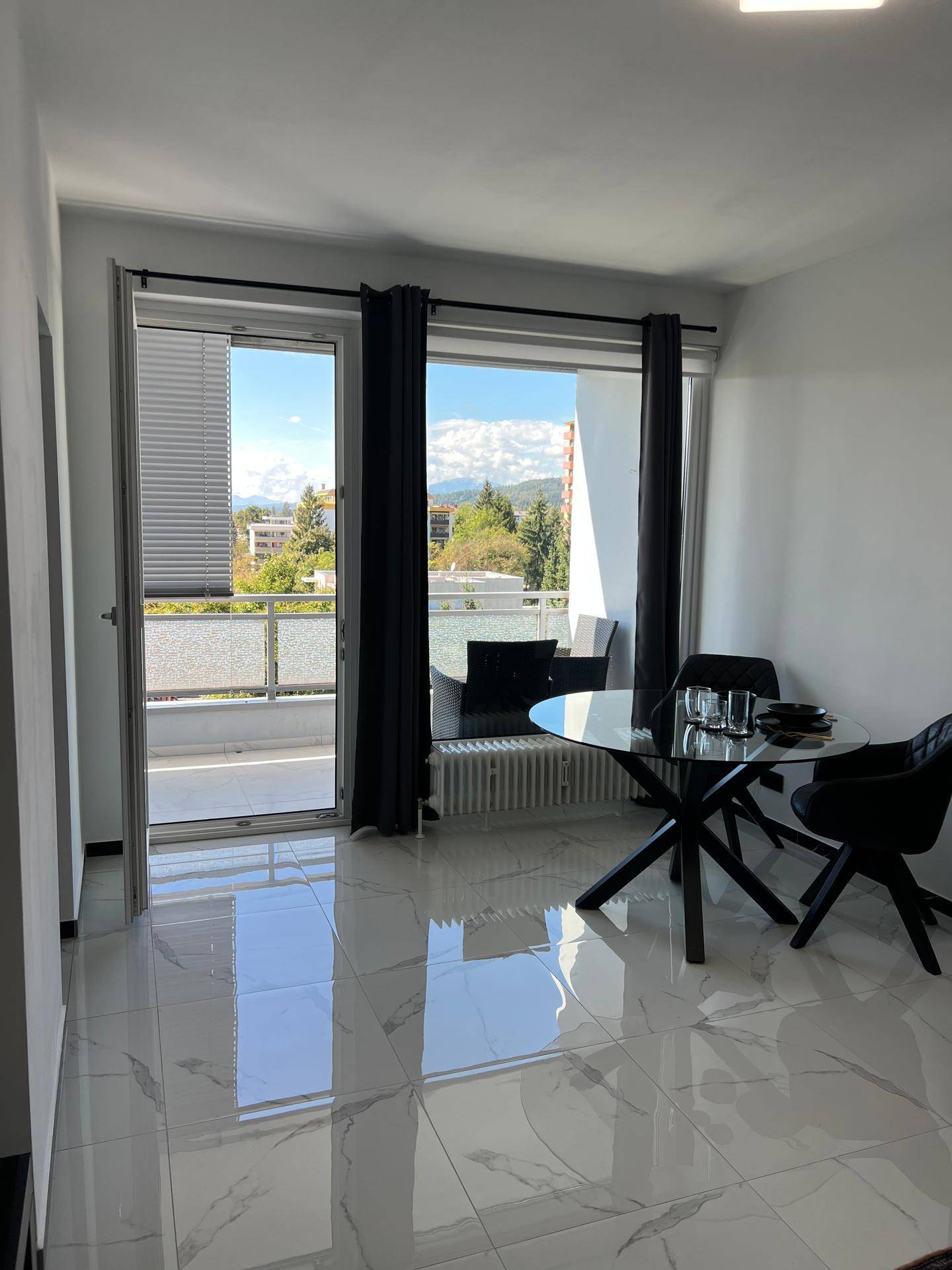 Heller Essbereich mit Glastisch und großem Fenster, das Zugang zum Balkon bietet.
