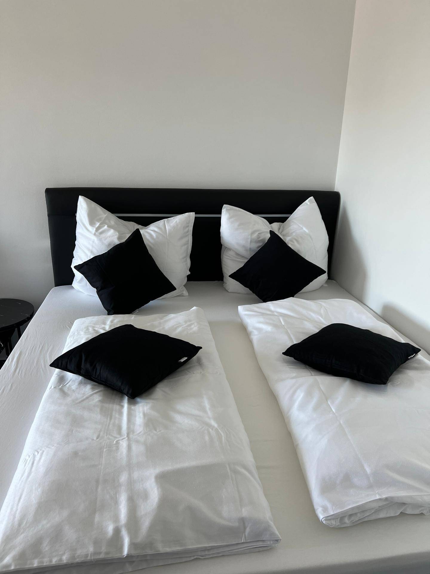Modernes Schlafzimmer mit einem großen Bett, weißen Laken und schwarzen Kissen auf dem Fliesenboden.