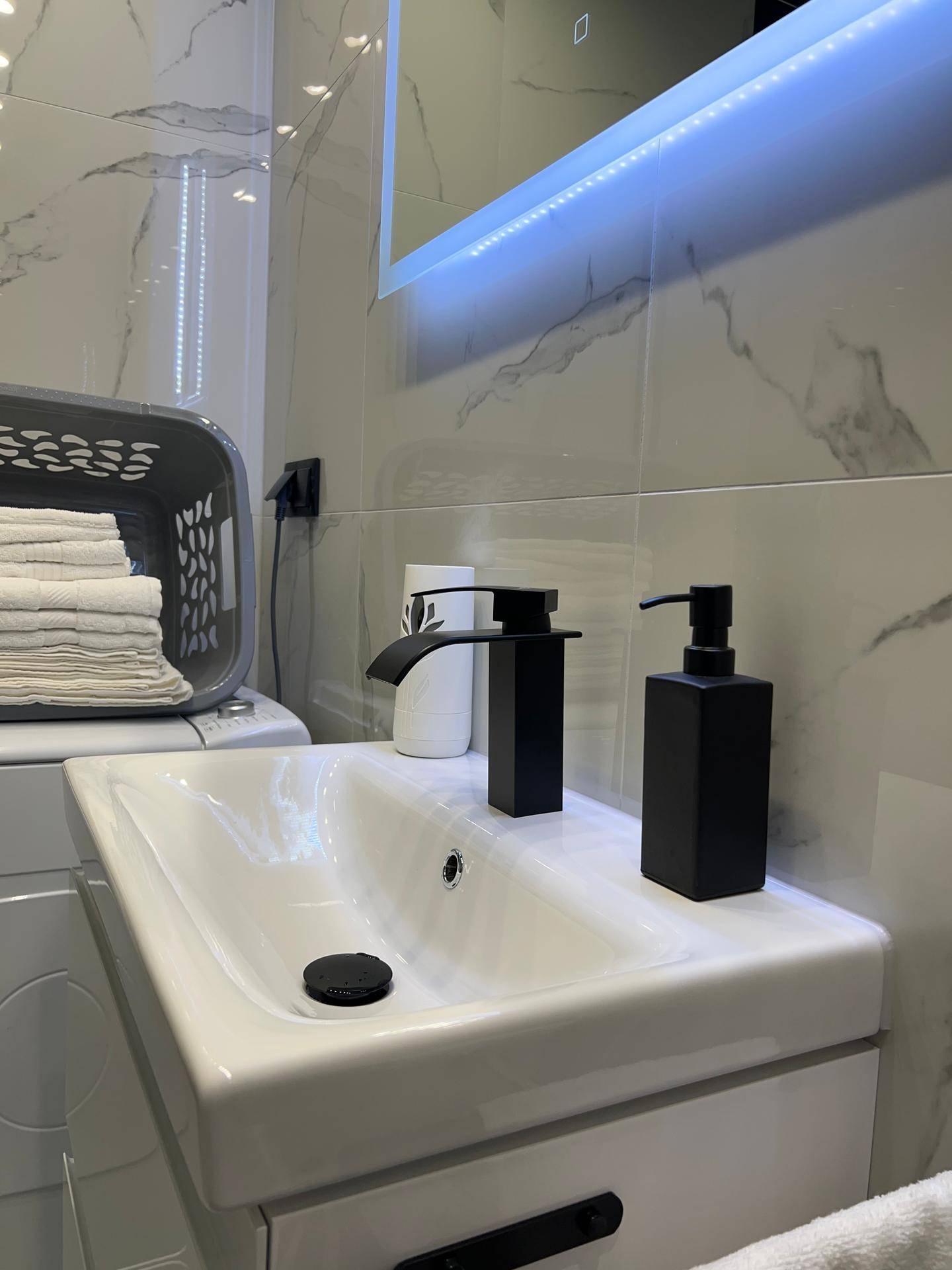 Nahaufnahme des modernen Waschbeckens mit schwarzem Wasserhahn und Seifenspender im Badezimmer.