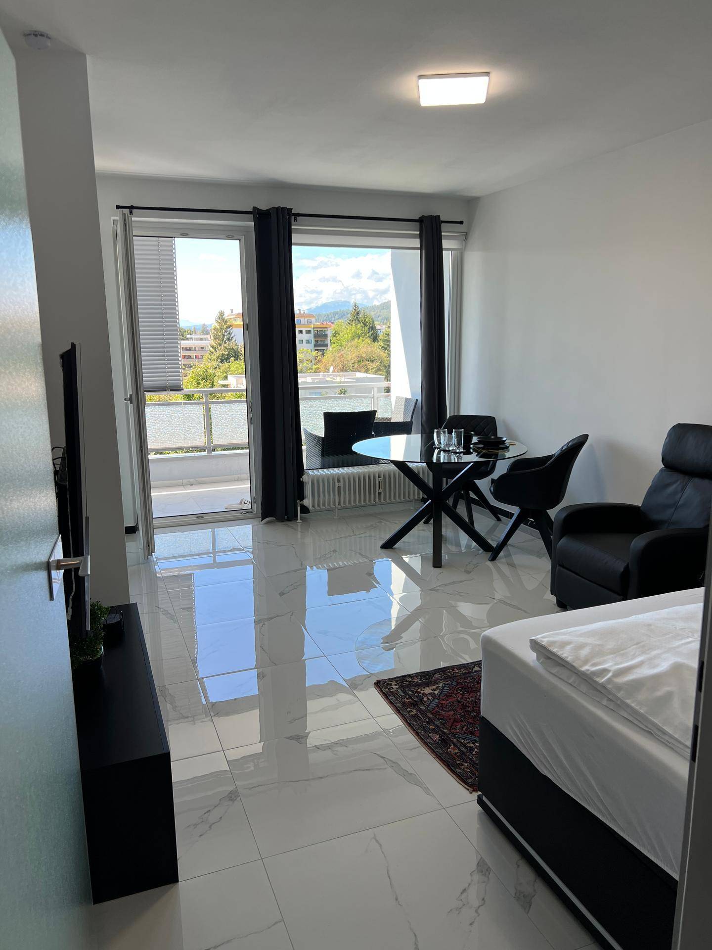 Offener Wohnbereich mit Schlafgelegenheit, Esstisch und Zugang zum sonnigen Balkon.