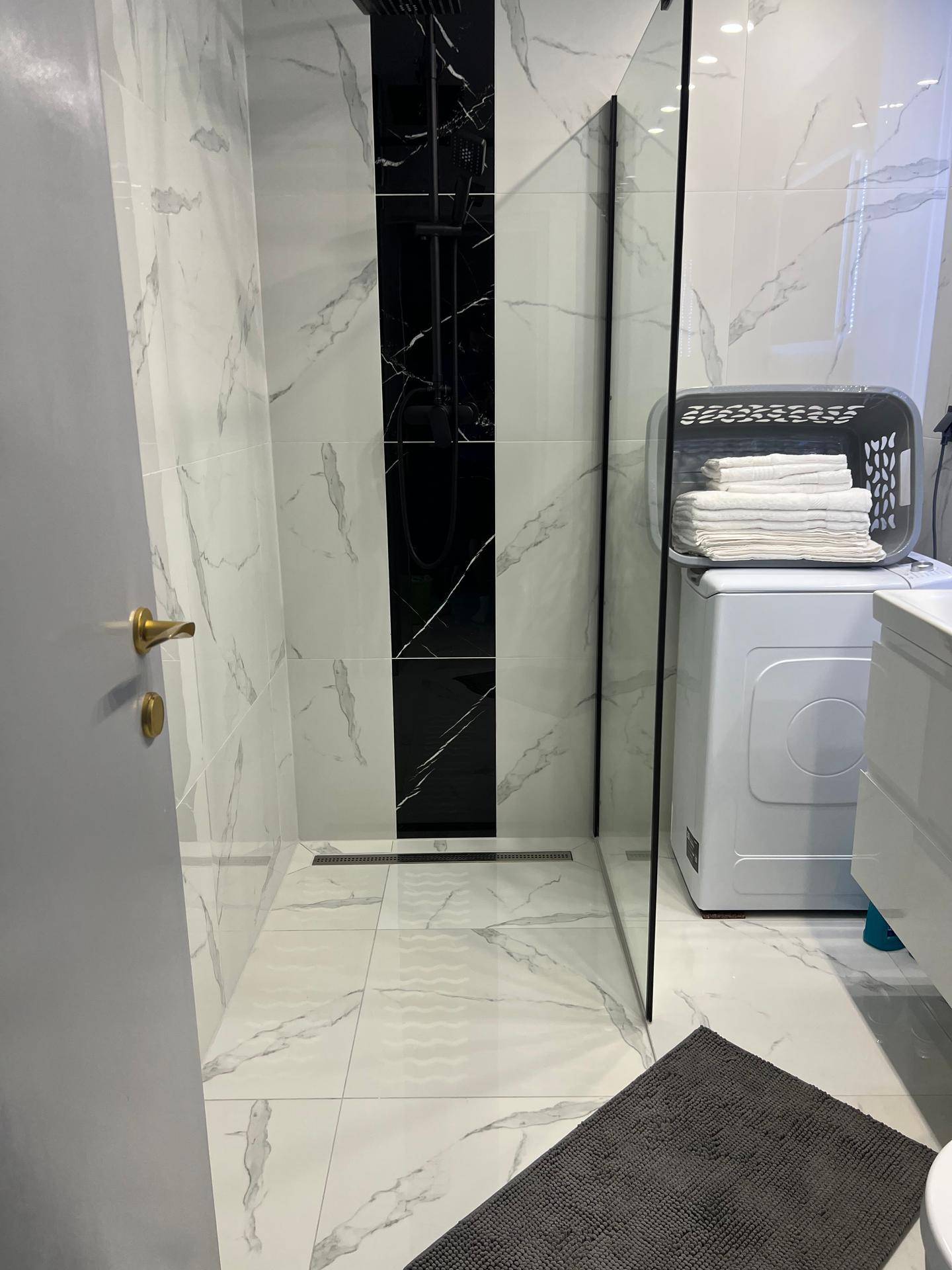 Modernes Badezimmer mit begehbarer Dusche, eleganten Marmorfliesen und einer Waschmaschine.