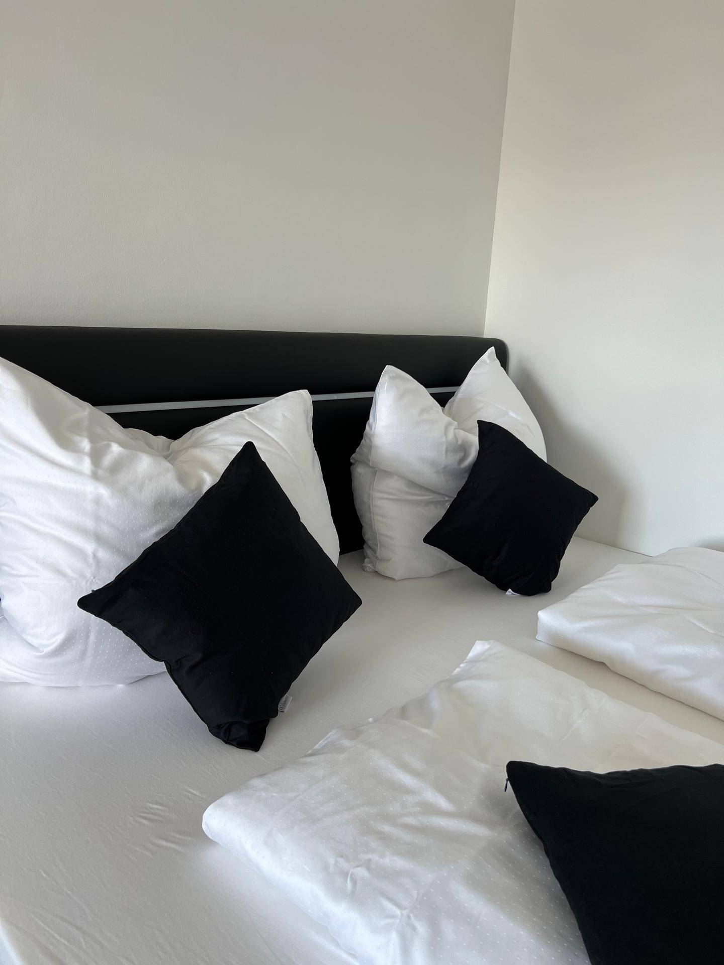 Nahaufnahme des Bettes mit weißen Laken und schwarzen Kissen in einem hellen Schlafzimmer.