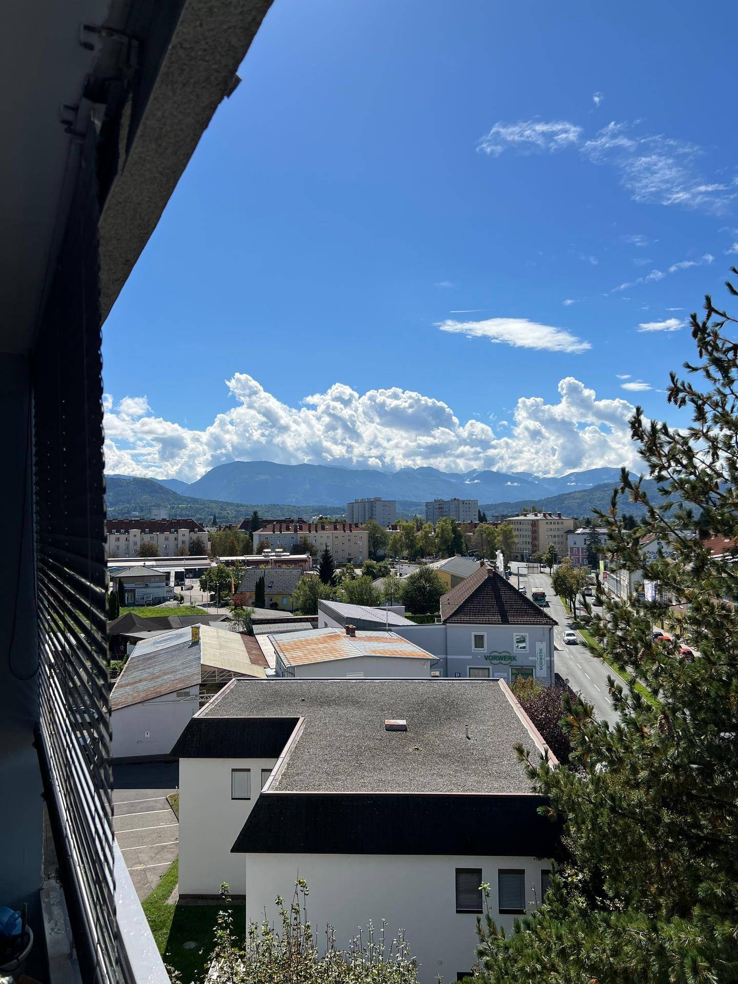 Panoramablick vom Balkon auf die Stadt und die umliegenden Berge unter blauem Himmel.