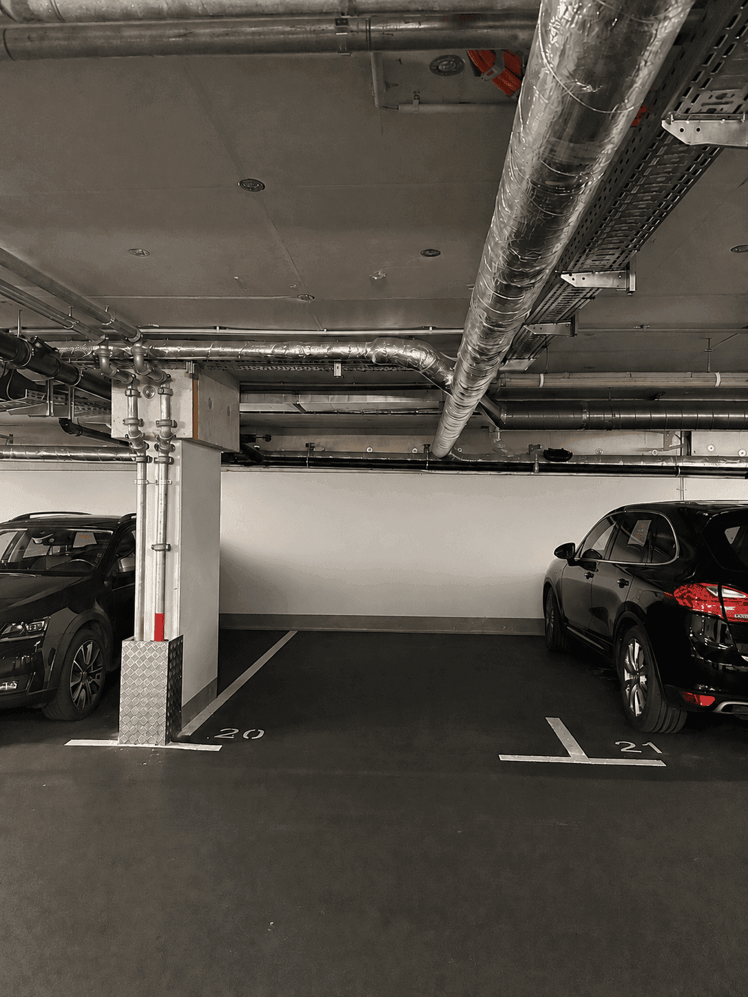Detailansicht einer Tiefgarage mit zwei Parkplätzen und sichtbaren Installationen an der Decke.