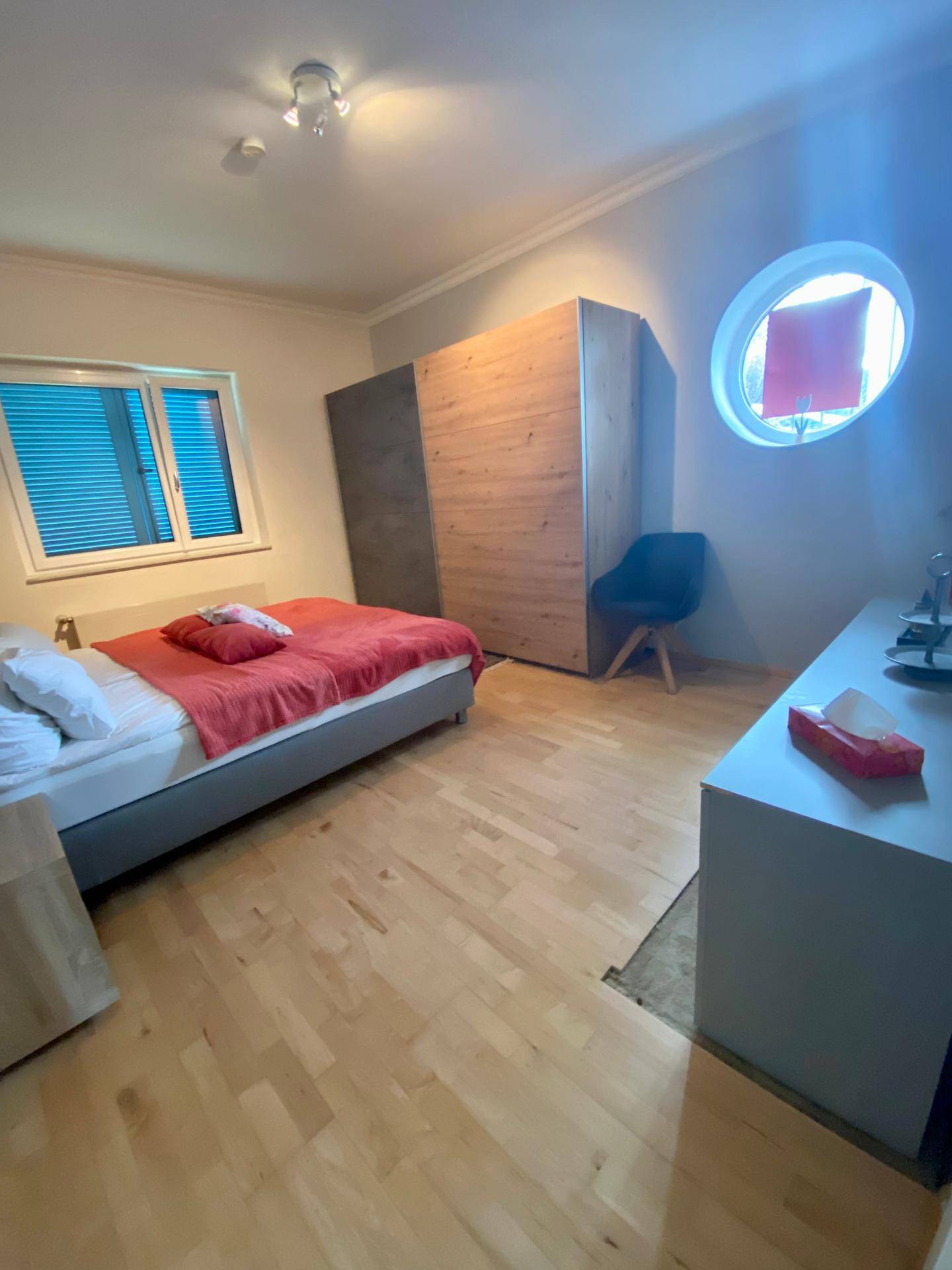 Schlafzimmer mit Holzboden, Doppelbett und runden sowie rechteckigen Fenstern.