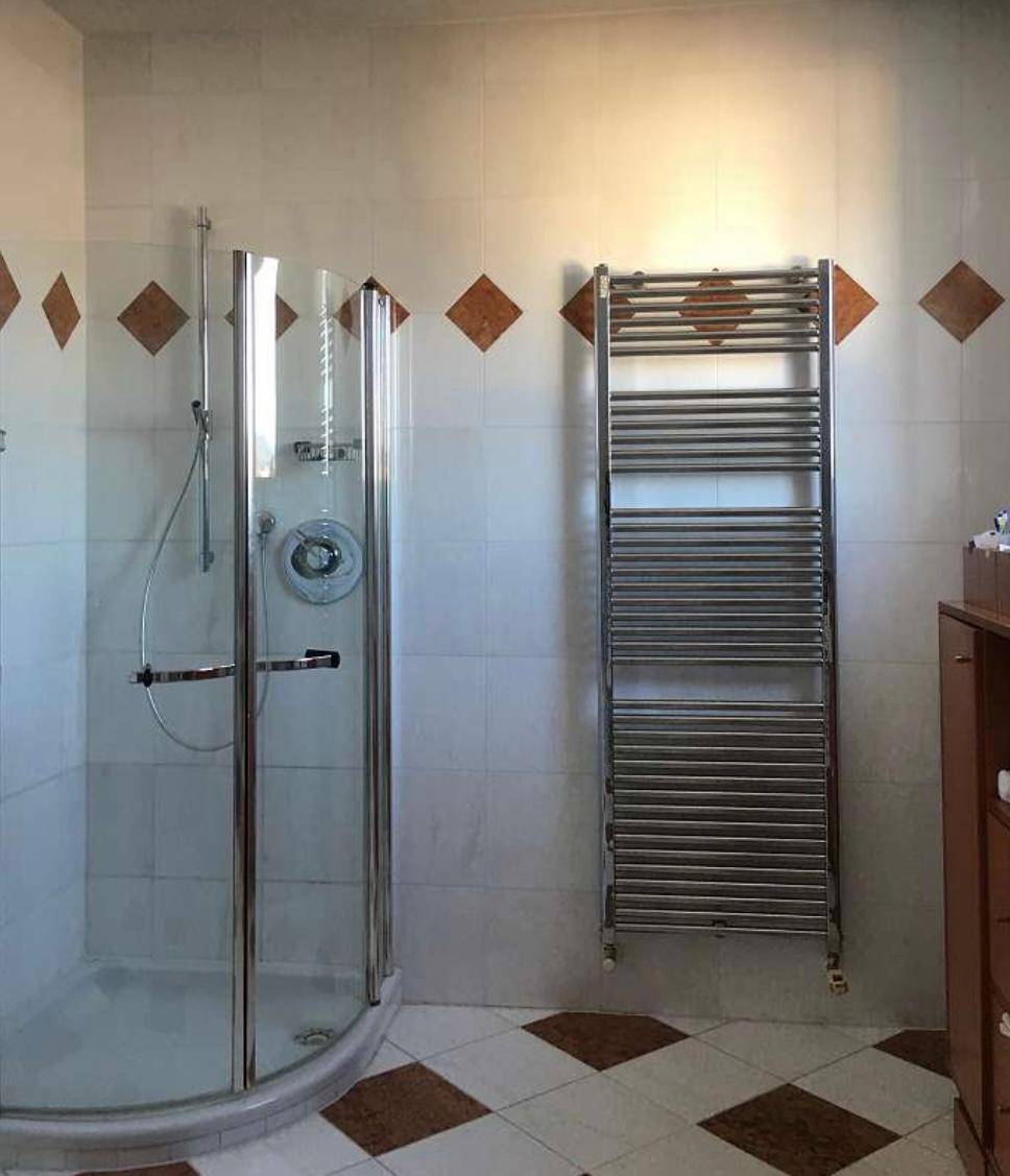 Badezimmer mit Duschkabine, beheiztem Handtuchhalter und Fliesen in Weiß und Braun.