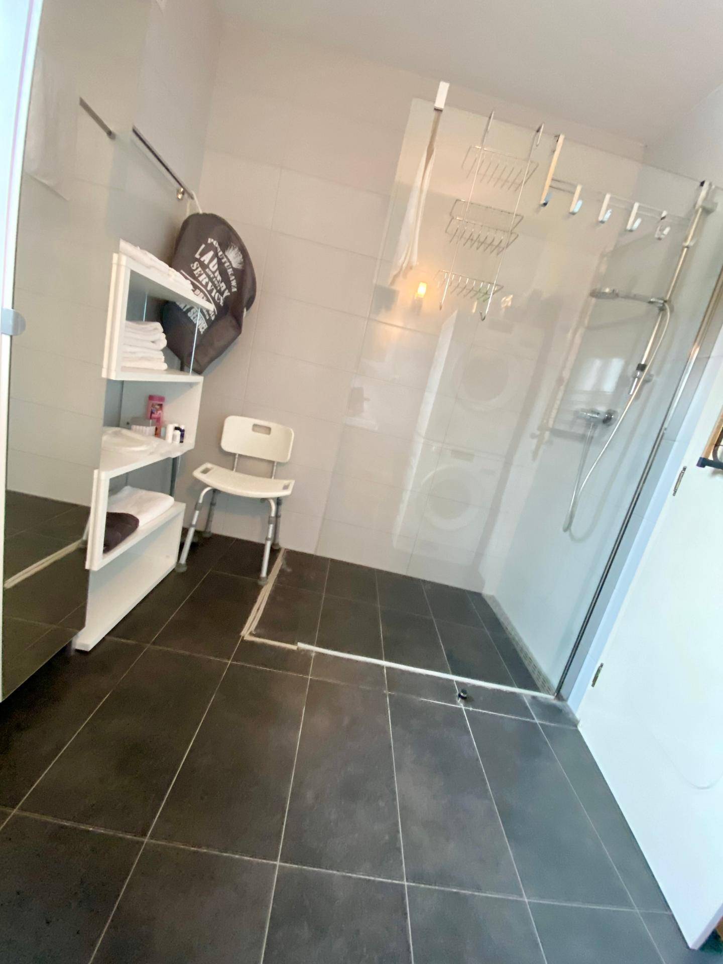 Geräumiges Badezimmer mit ebenerdiger Dusche, hellen Wandfliesen und dunklem Boden.