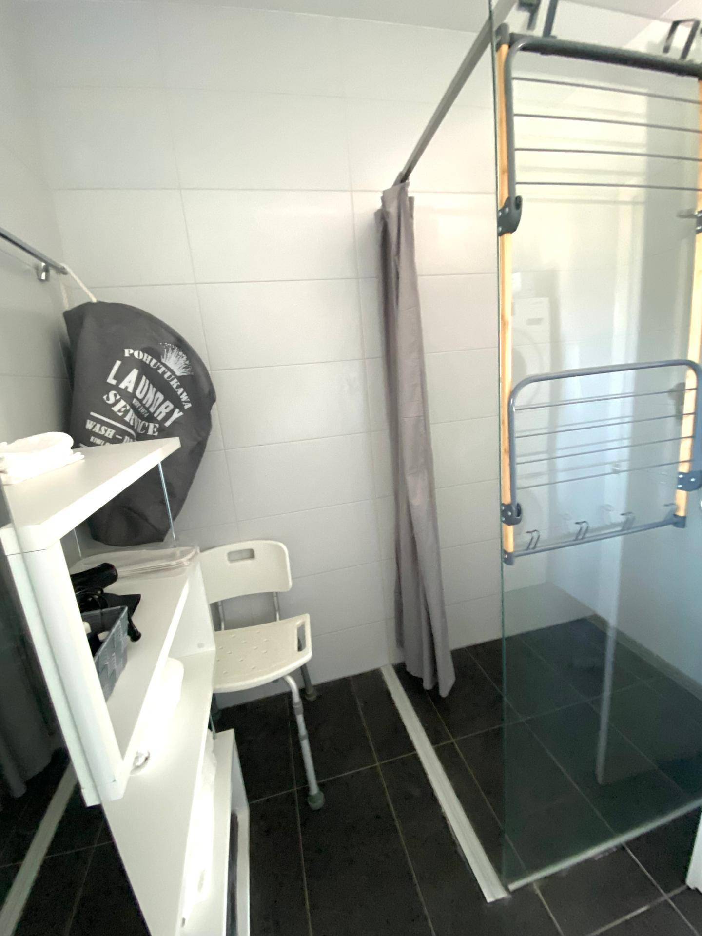 Praktischer Waschraum mit Dusche, Wäscheständer und Fliesenboden.
