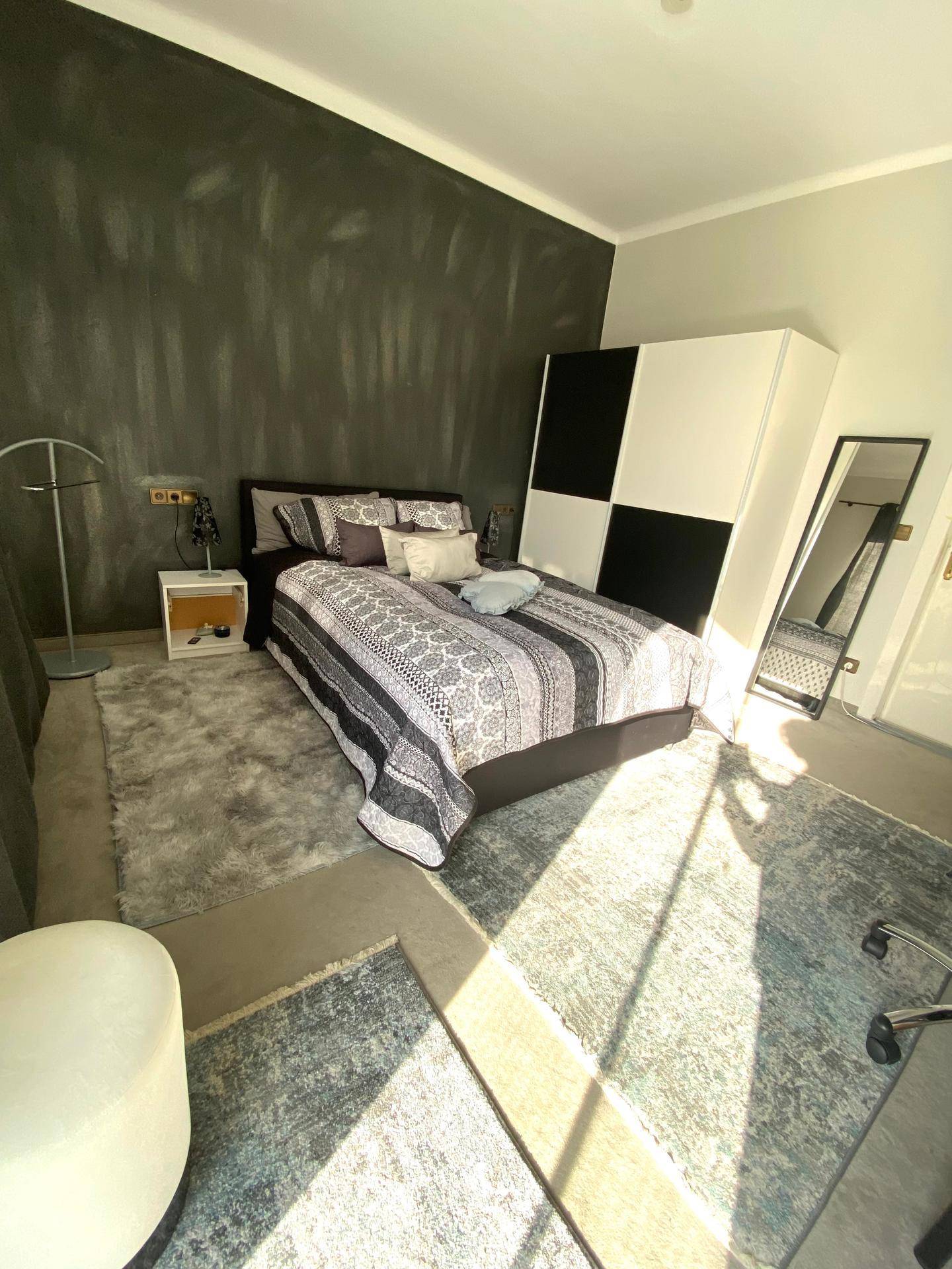 Schlafzimmer mit Doppelbett, dunkler Akzentwand und großem Spiegel.