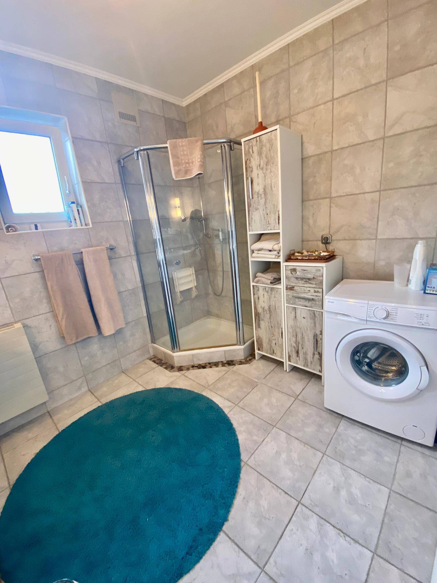 Badezimmer mit Dusche, Waschmaschine und Fliesenboden in neutralen Farben.