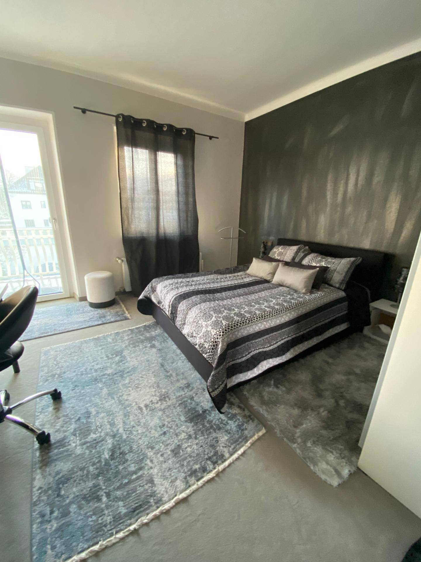 Modernes Schlafzimmer mit Doppelbett, Schreibtisch und einer dunklen Akzentwand, die Tiefe verleiht.