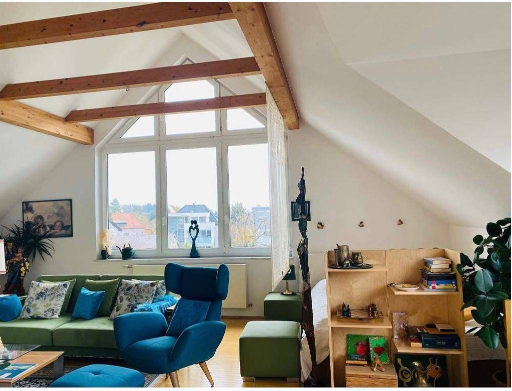 Helles Wohnzimmer im Dachgeschoss mit Holzbalken, großen Fenstern und moderner Einrichtung.