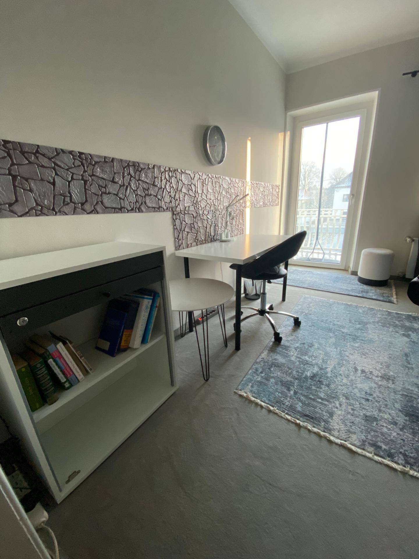 Helles Schlafzimmer mit Schreibtisch, Regal und Zugang zu einem Balkon, ideal für Home-Office.