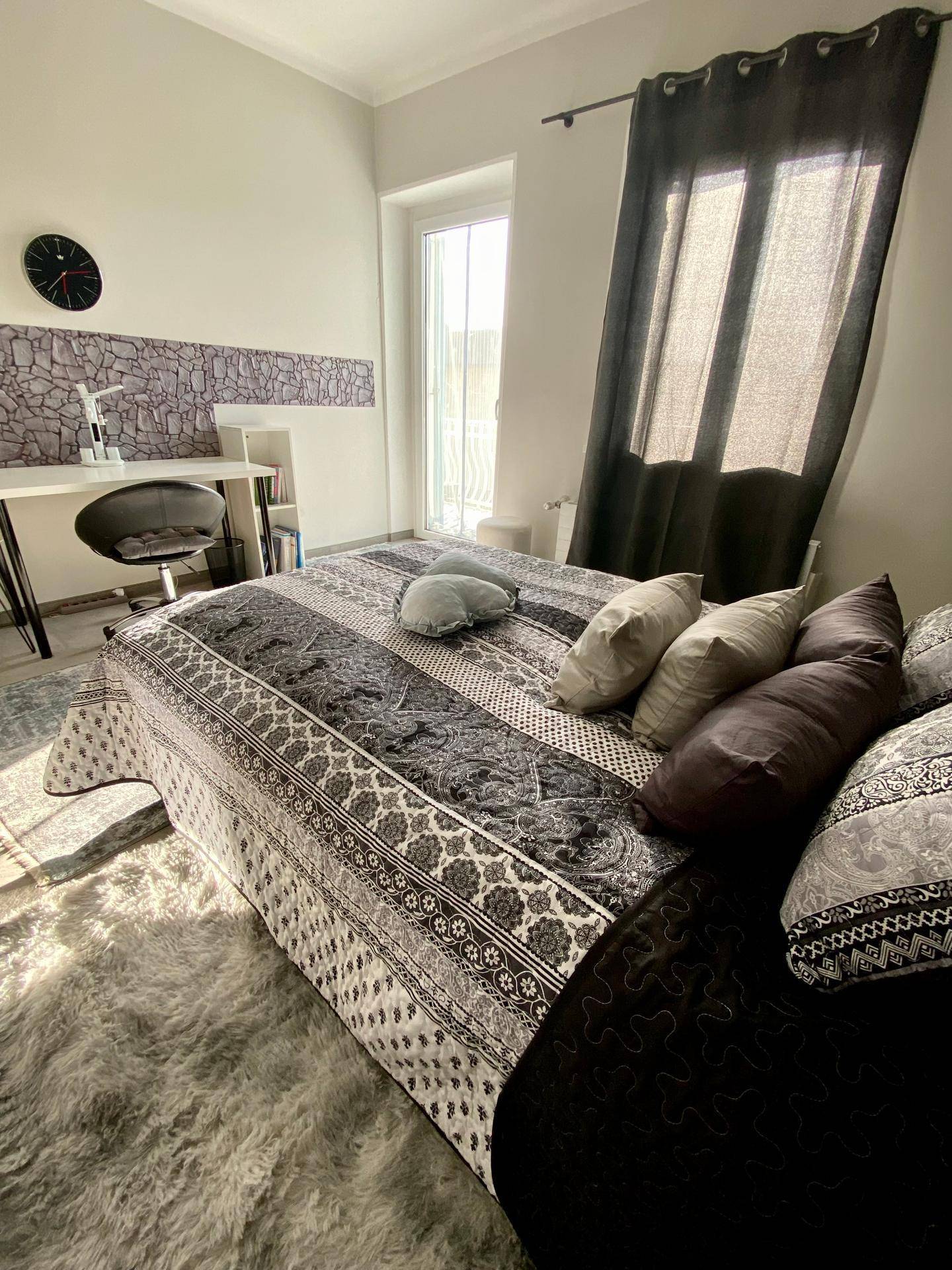 Gemütliches Schlafzimmer mit großem Bett, dekorativen Kissen und viel Tageslicht durch die Fenstertür.