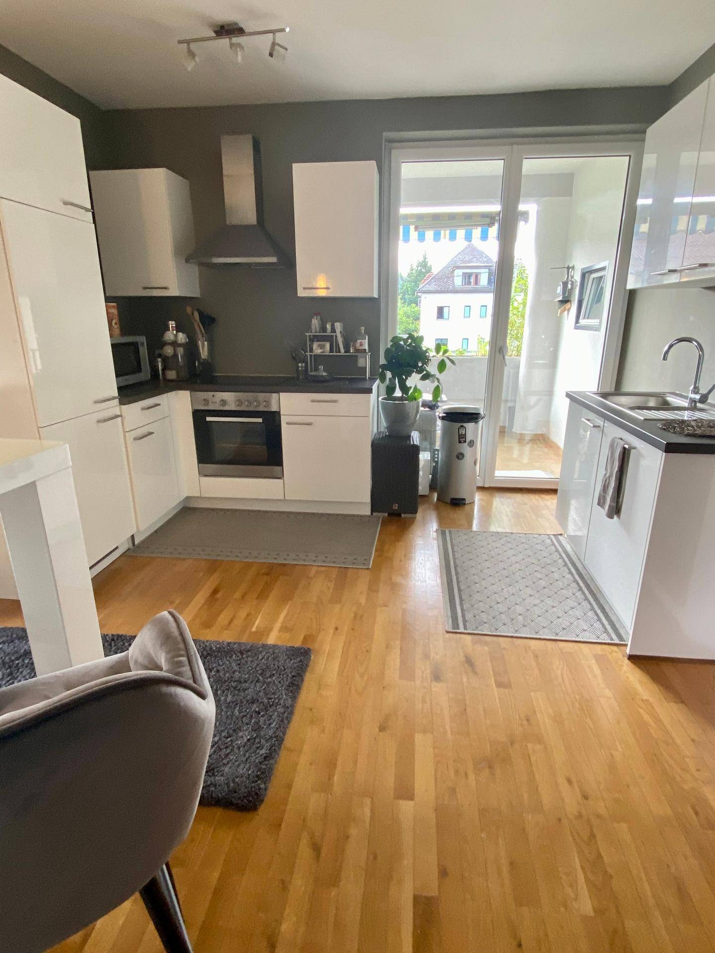 Helle Küche mit Zugang zum Balkon, ausgestattet mit modernen weißen Schränken und Holzboden.