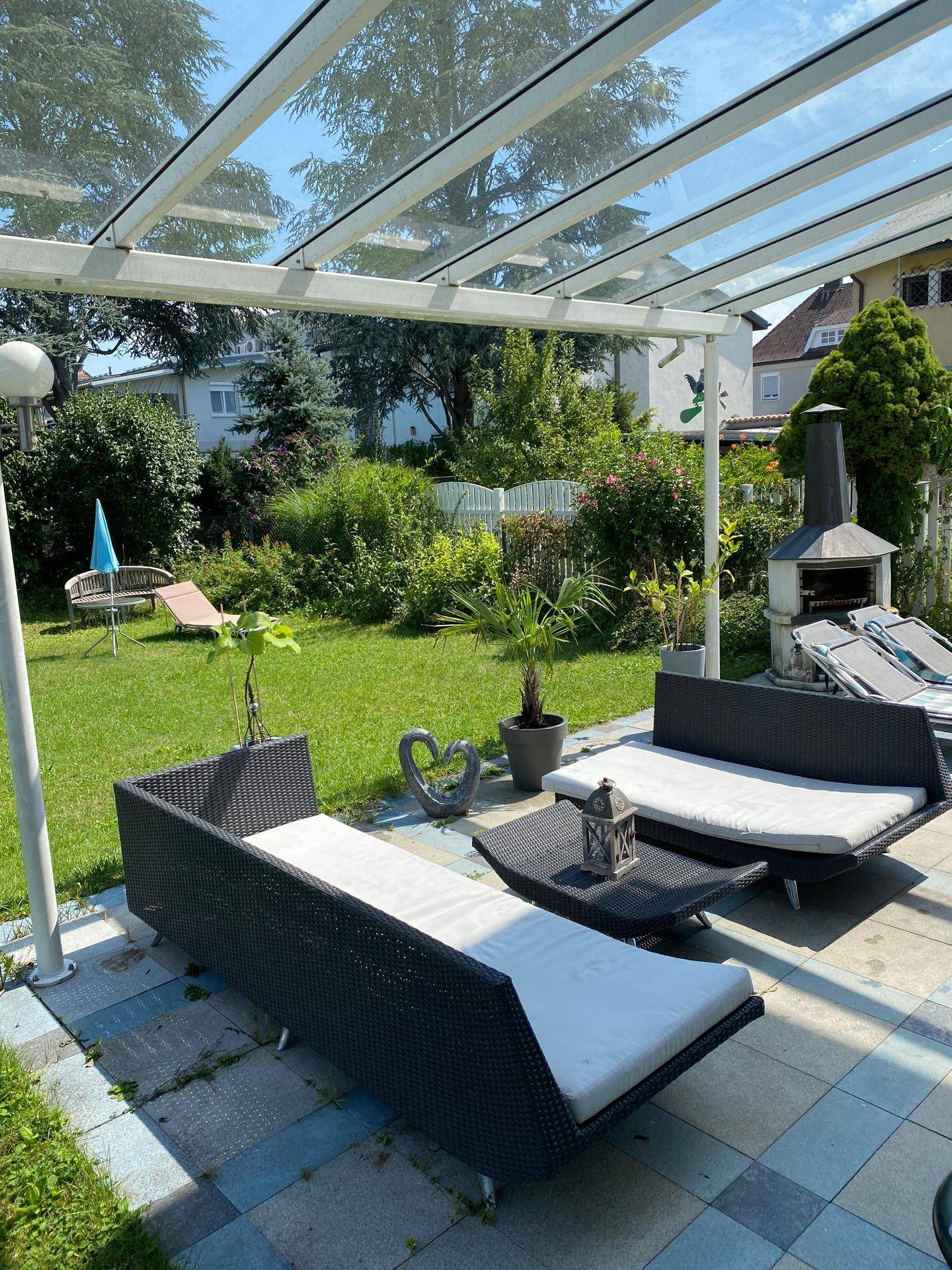 Überdachte Terrasse mit Lounge-Möbeln und integriertem Grillbereich im Garten.