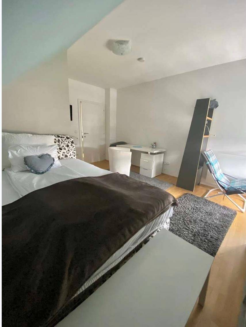 Schlafzimmer im Dachgeschoss mit Bett, Schreibtisch und Fenster für Tageslicht.