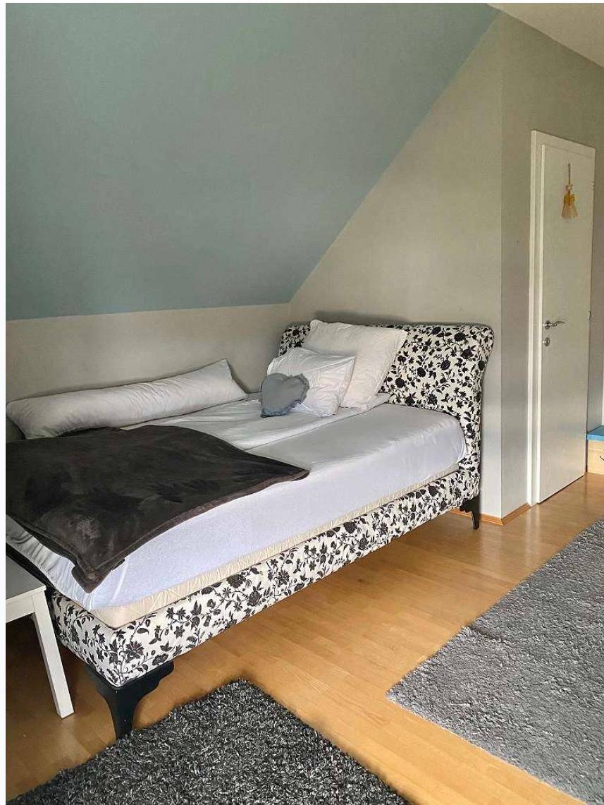 Schlafzimmer im Dachgeschoss mit gemustertem Bett, Holzboden und schräger Decke.