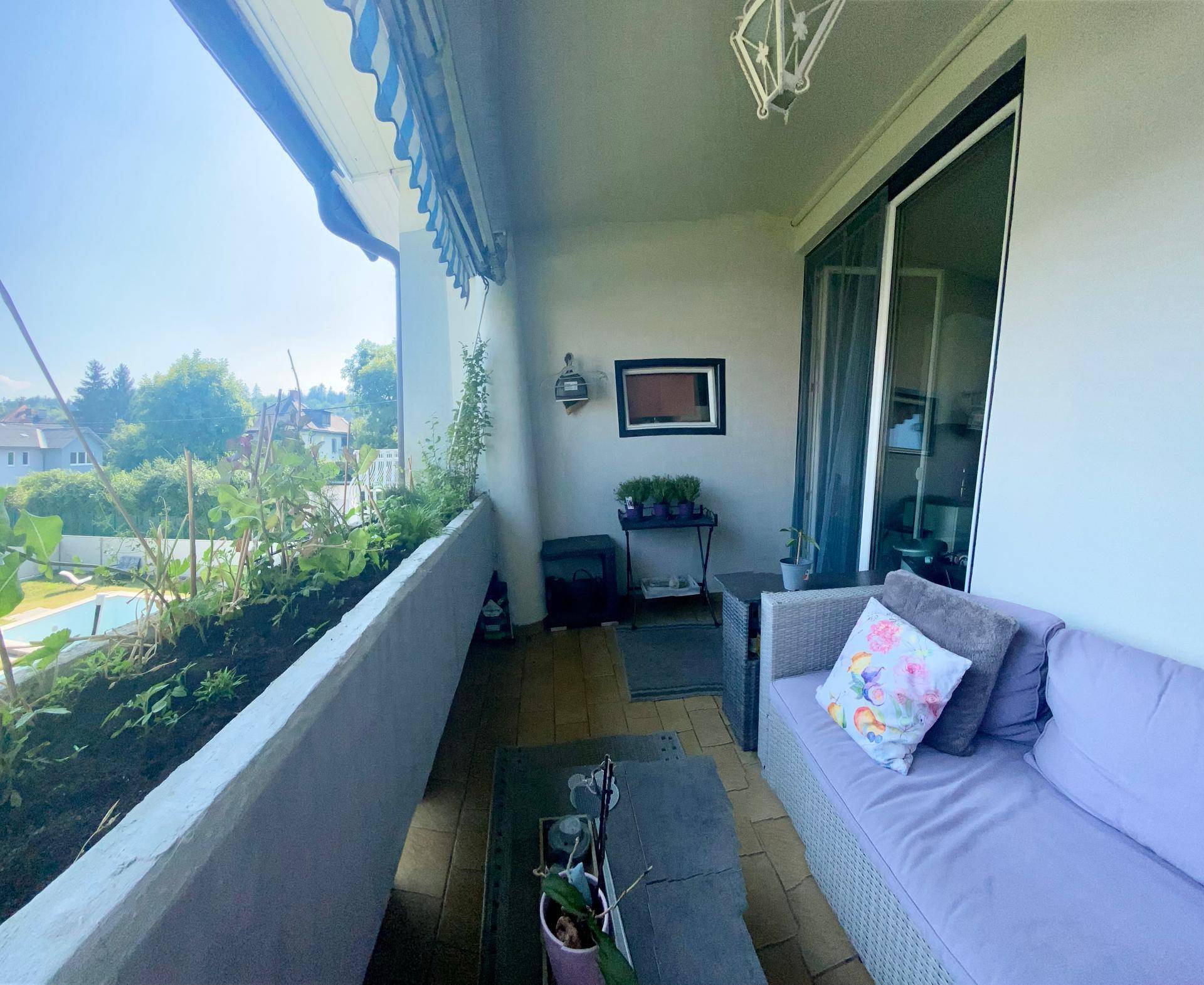 Langer Balkon mit Pflanzenkübeln, Sitzbereich und Blick auf die Umgebung, sonnig.