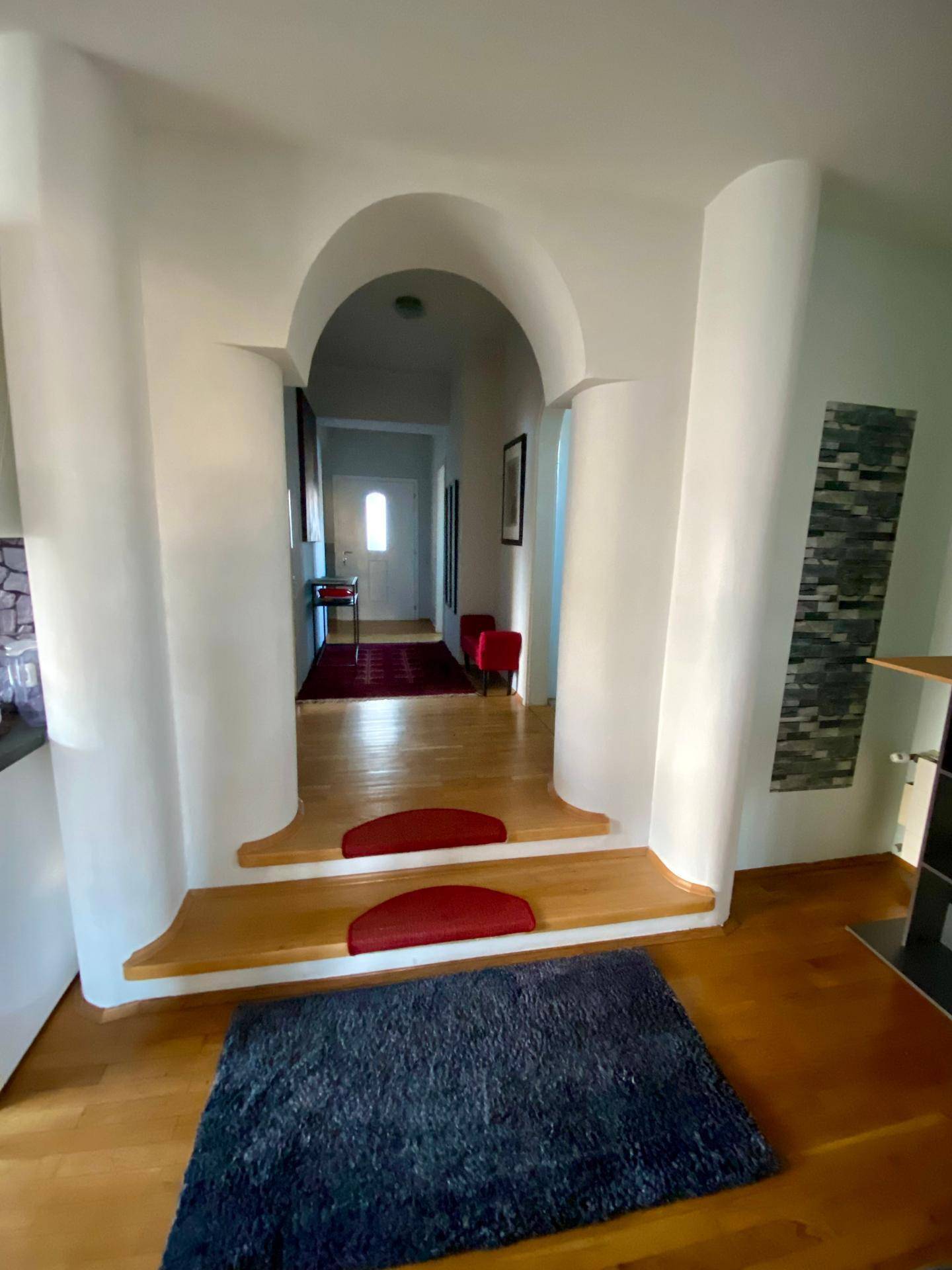 Heller Flur mit eleganten Bögen und Holzstufen, die zu einem weiteren Bereich des Hauses führen.