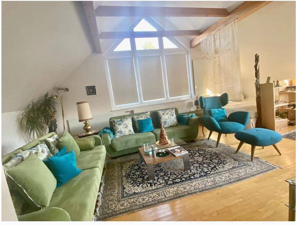 Geräumiges Wohnzimmer im Dachgeschoss mit Holzbalken, großen Fenstern und bequemen Sofas.