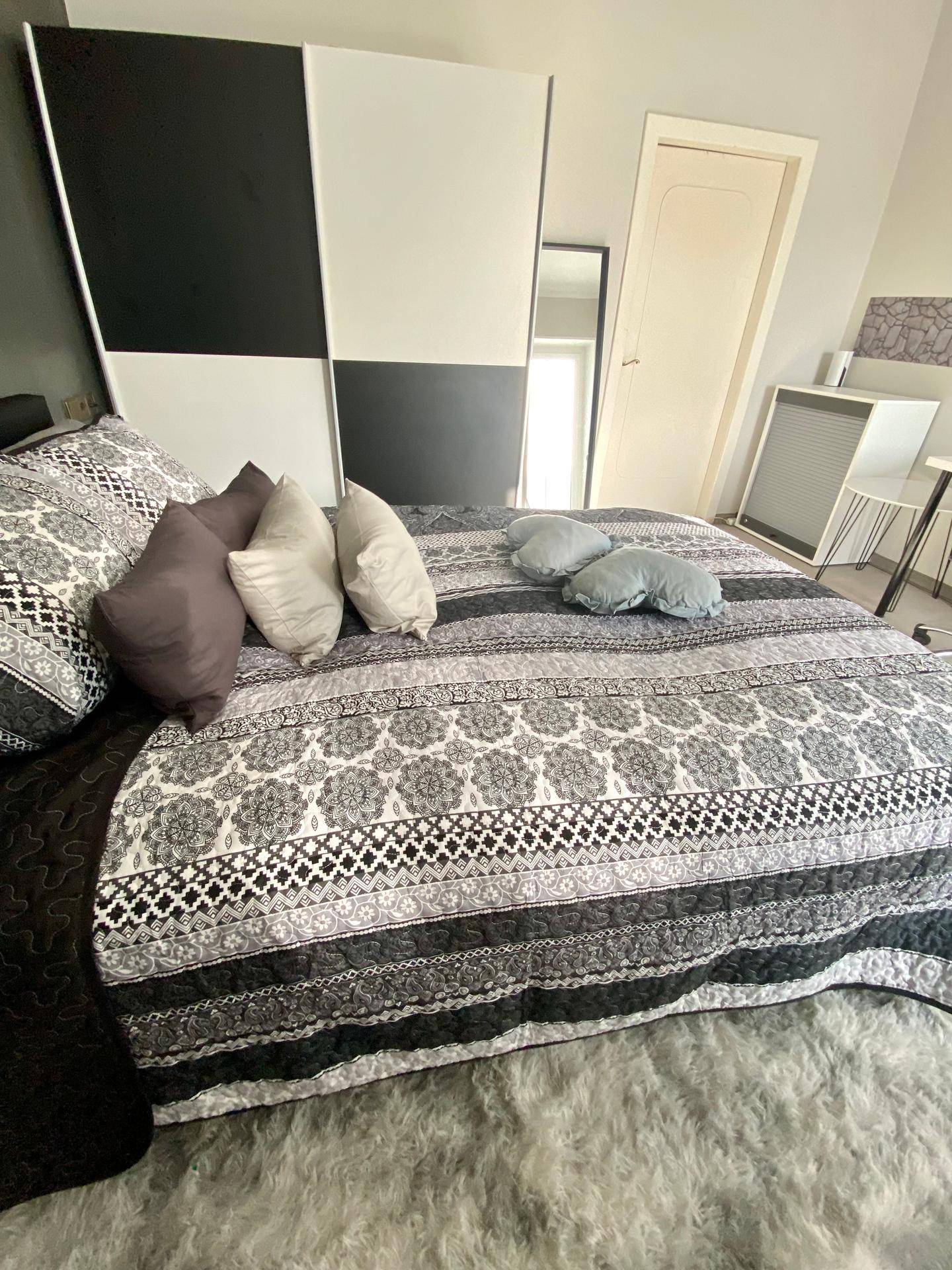 Schlafzimmer mit großem Bett, flauschigem Teppich und einem modernen schwarz-weißen Kleiderschrank.
