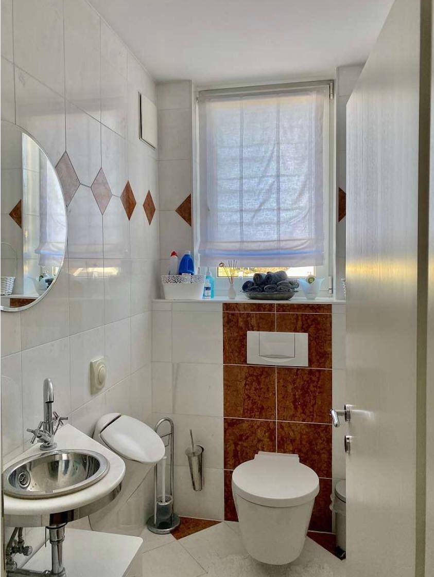 Kleines WC mit Fenster, wandhängender Toilette und modernem Waschbecken.