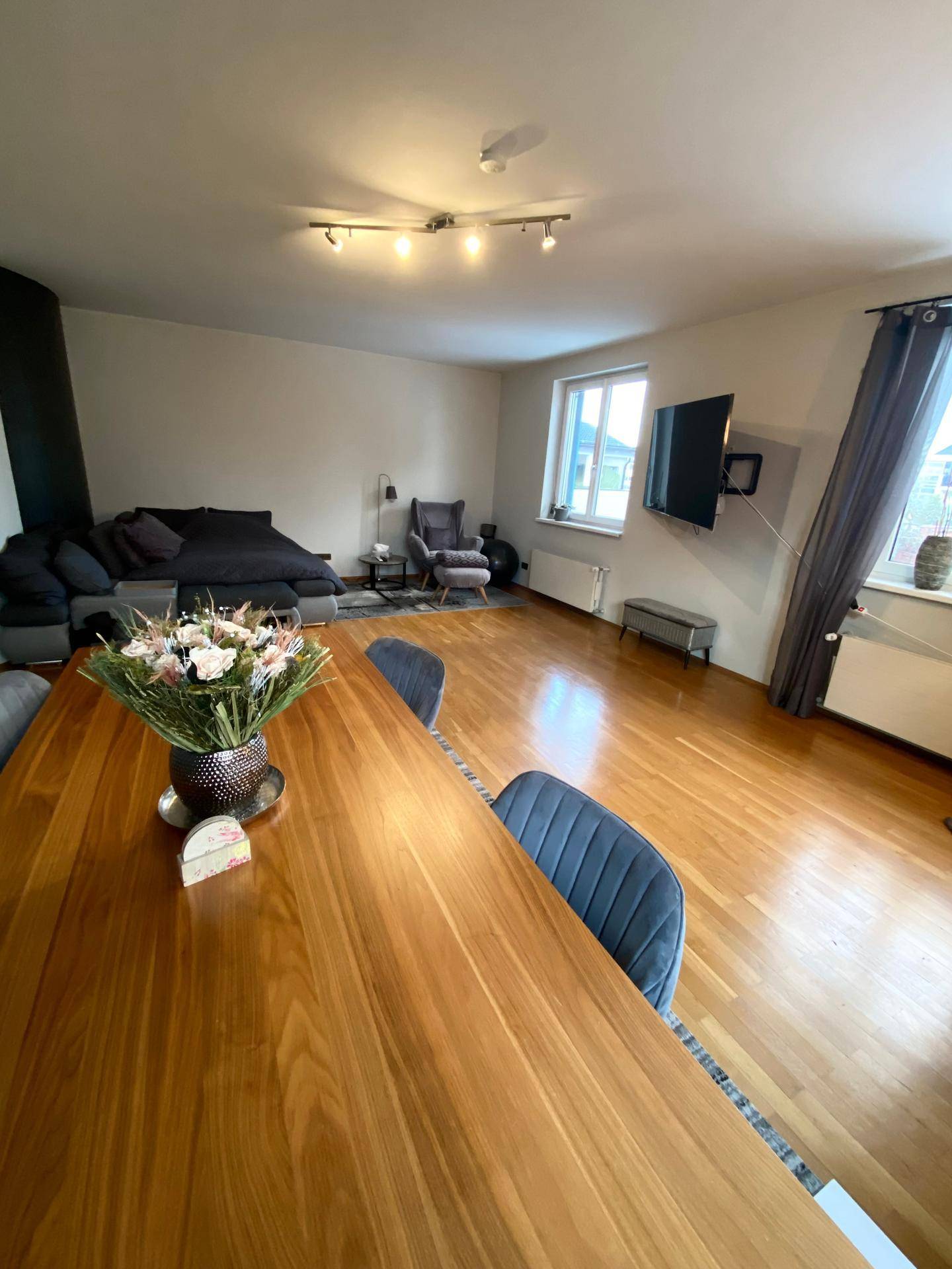 Geräumiger Wohn-Essbereich mit Holzboden, Esstisch und einem gemütlichen Sofa im Hintergrund.