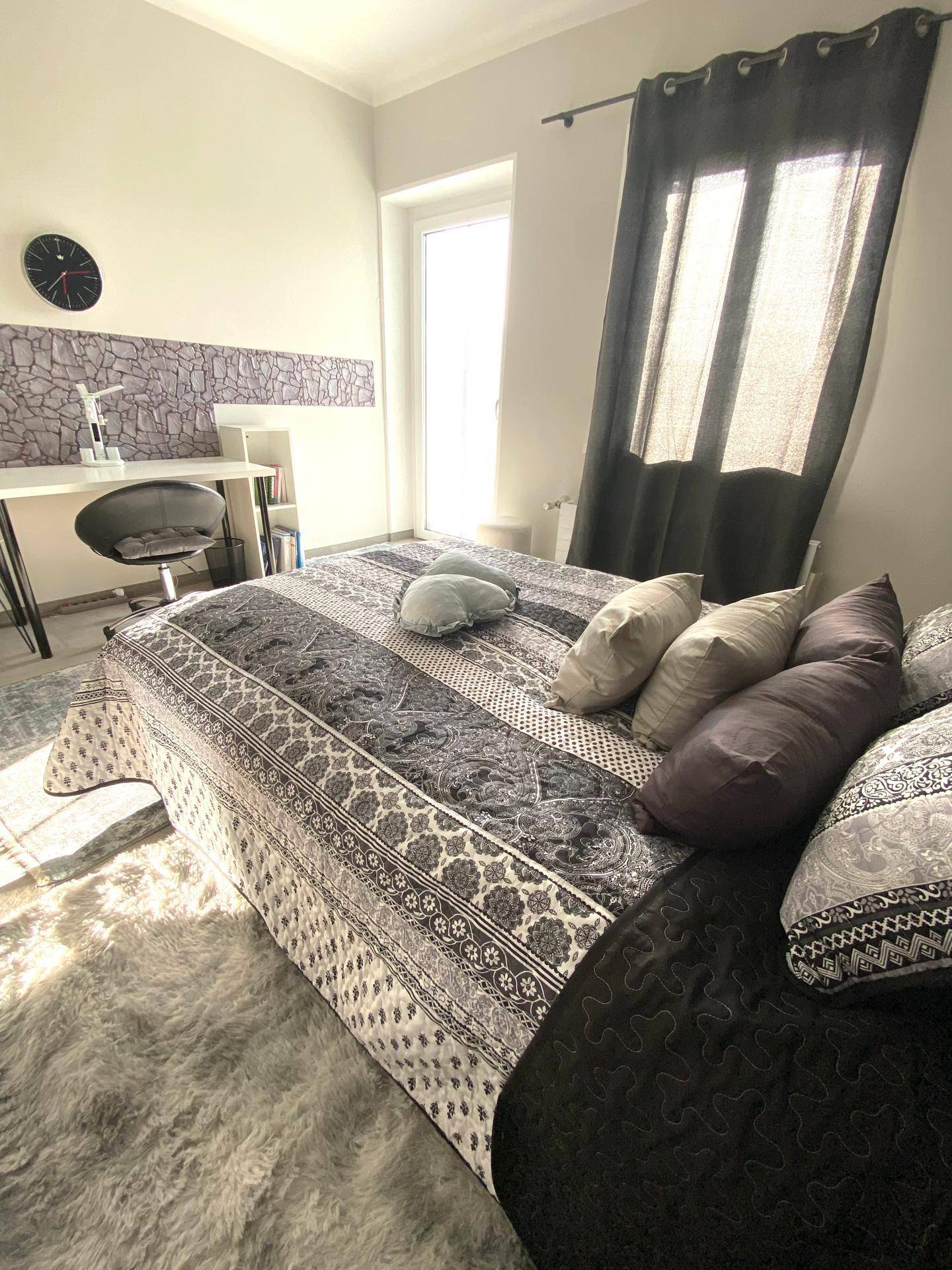 Helles Schlafzimmer mit Doppelbett, Schreibtisch und Zugang zu einem Außenbereich.