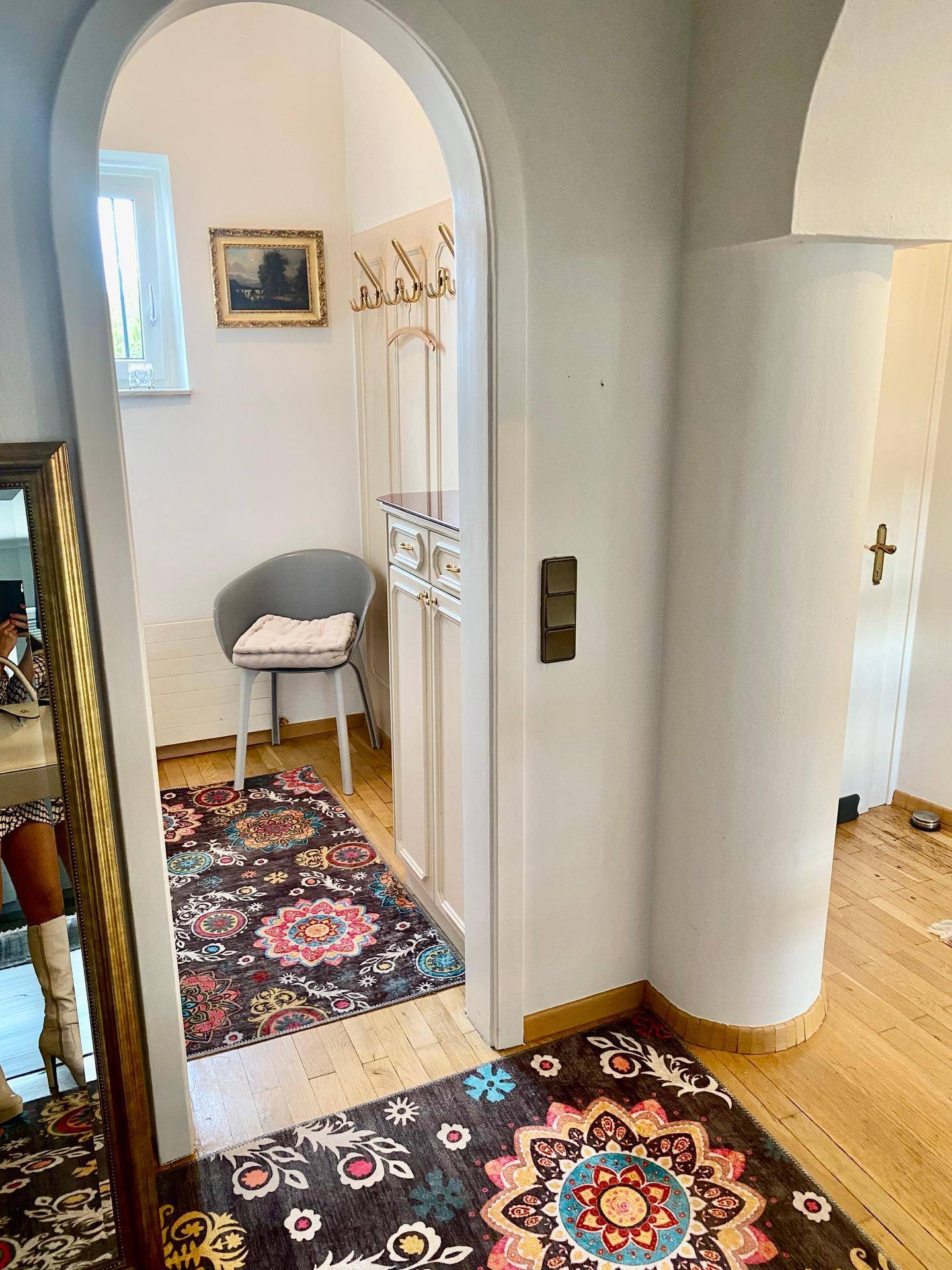 Eingangsbereich mit Holzboden, Garderobe und dekorativem Teppich.