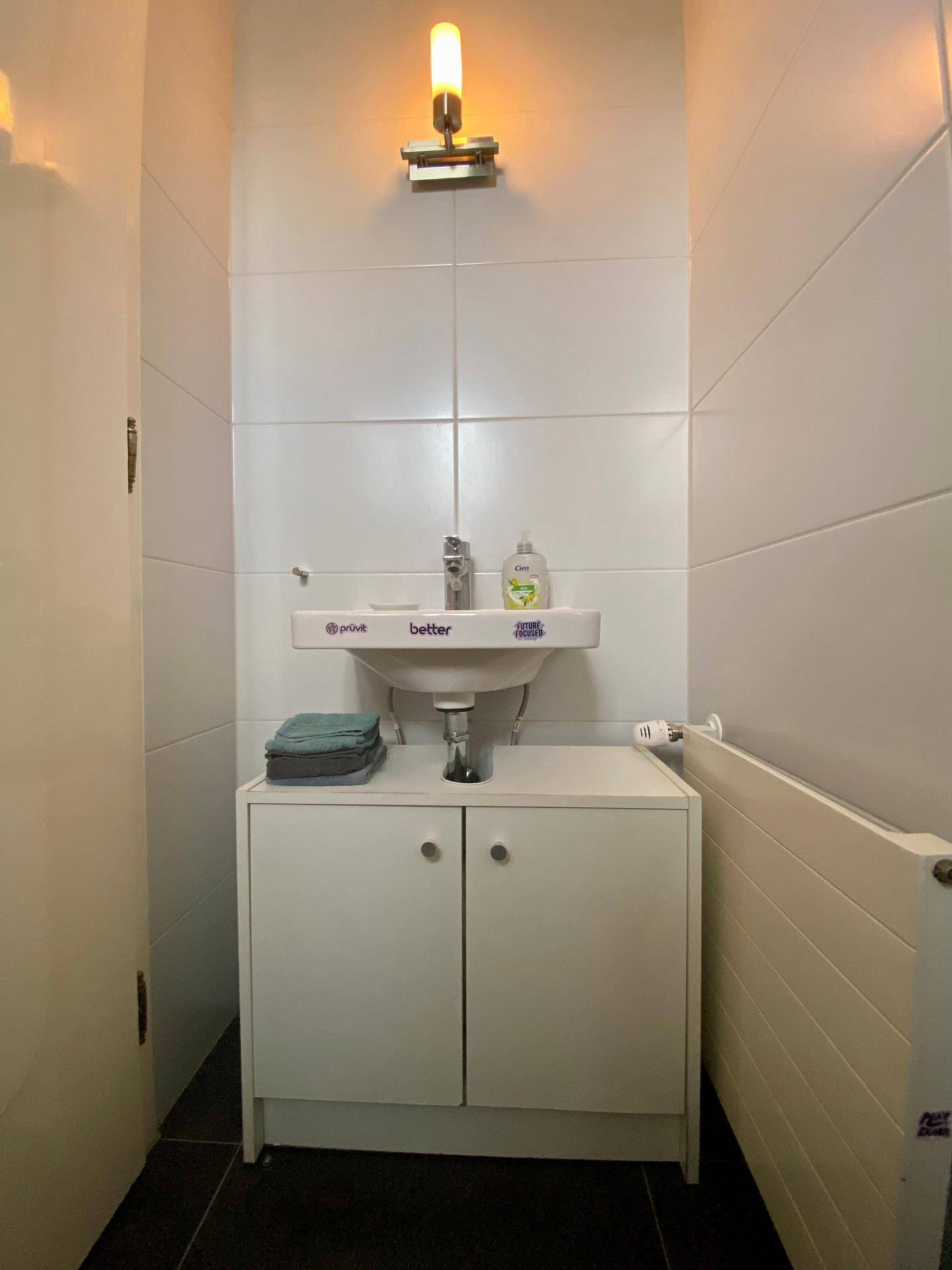 Kleines Gäste-WC mit Waschbecken, Unterschrank und Heizkörper, hell gefliest.