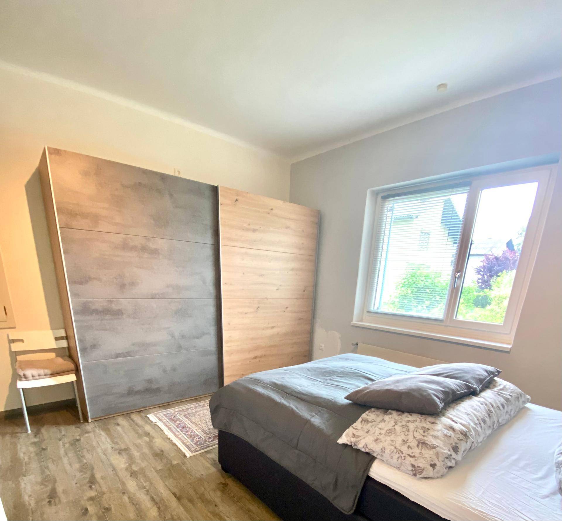 Schlafzimmer mit modernem Schiebetürenschrank, Bett und Fenster mit Blick ins Grüne.