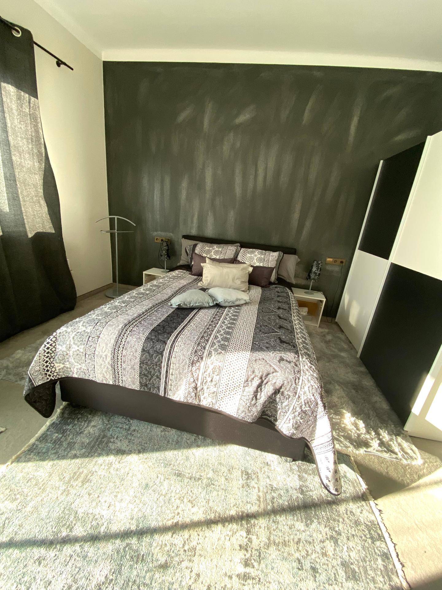 Modernes Schlafzimmer mit Doppelbett, dunkler Akzentwand und Teppichboden.