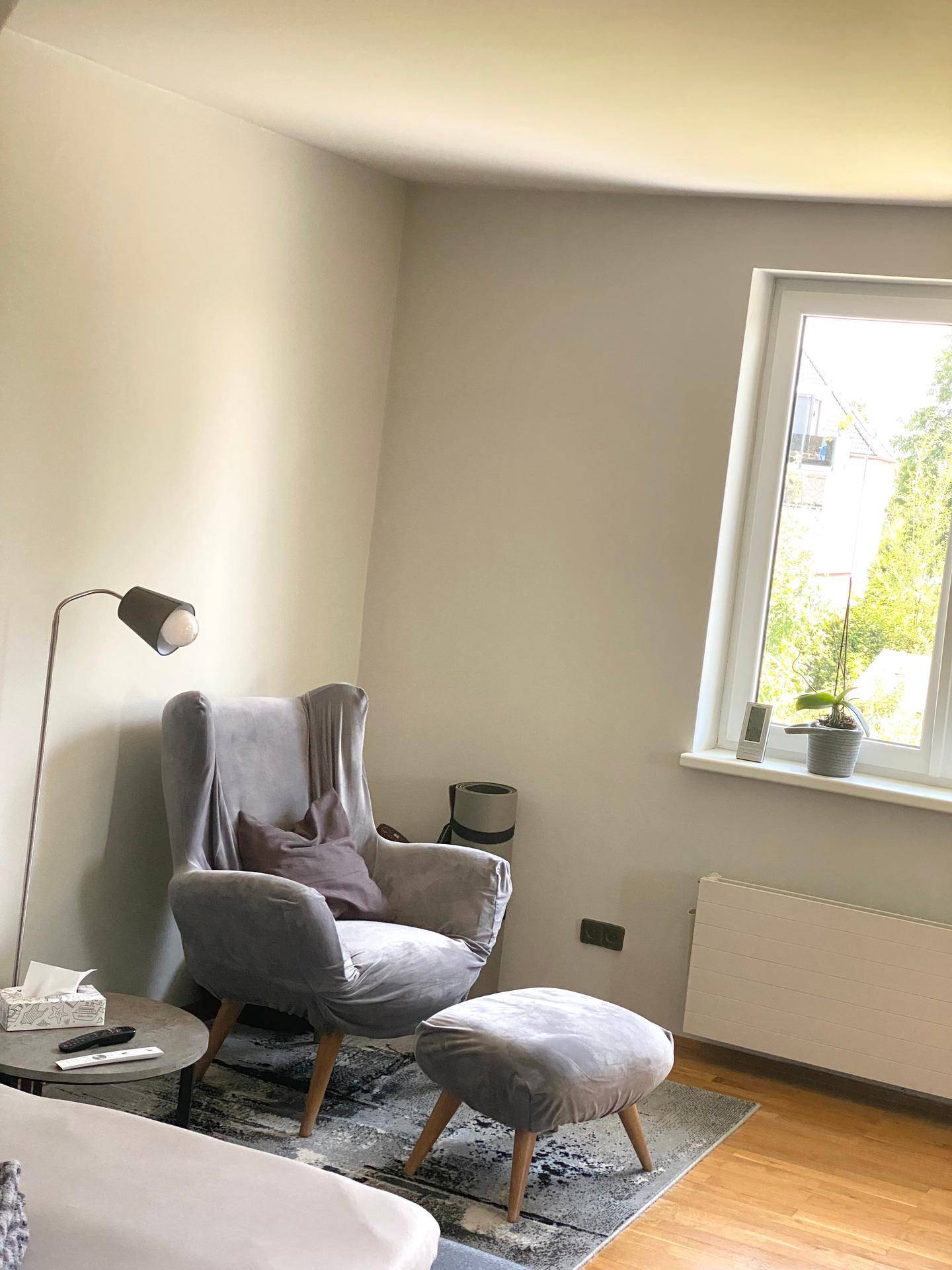 Helles Wohnzimmer mit Sessel, Stehlampe und Fenster für natürliches Licht.